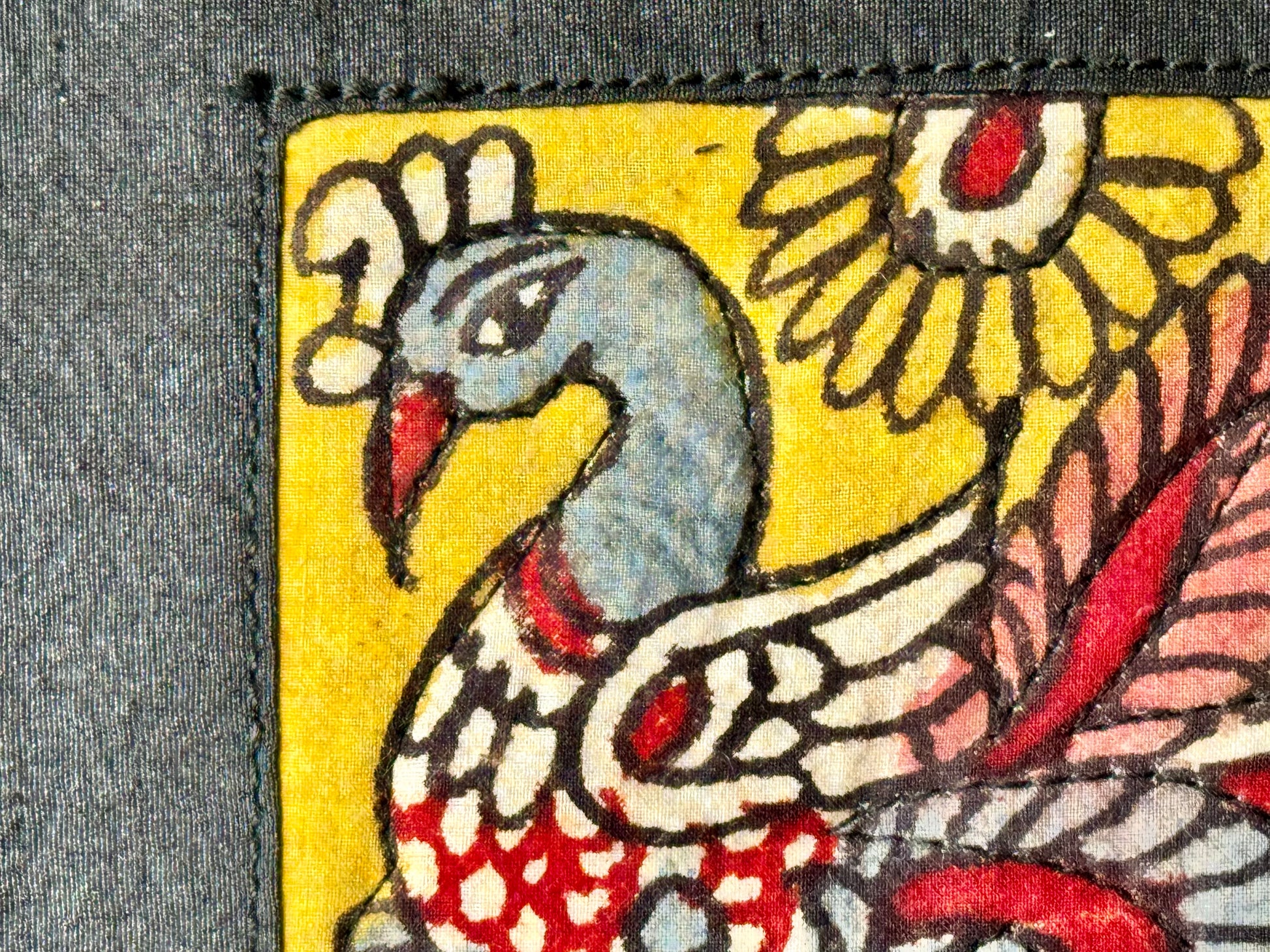 Close-up of a hand-painted makeup pouch with traditional Kalamkari art design featuring a bird and floral motifs in bright colors on a yellow background.