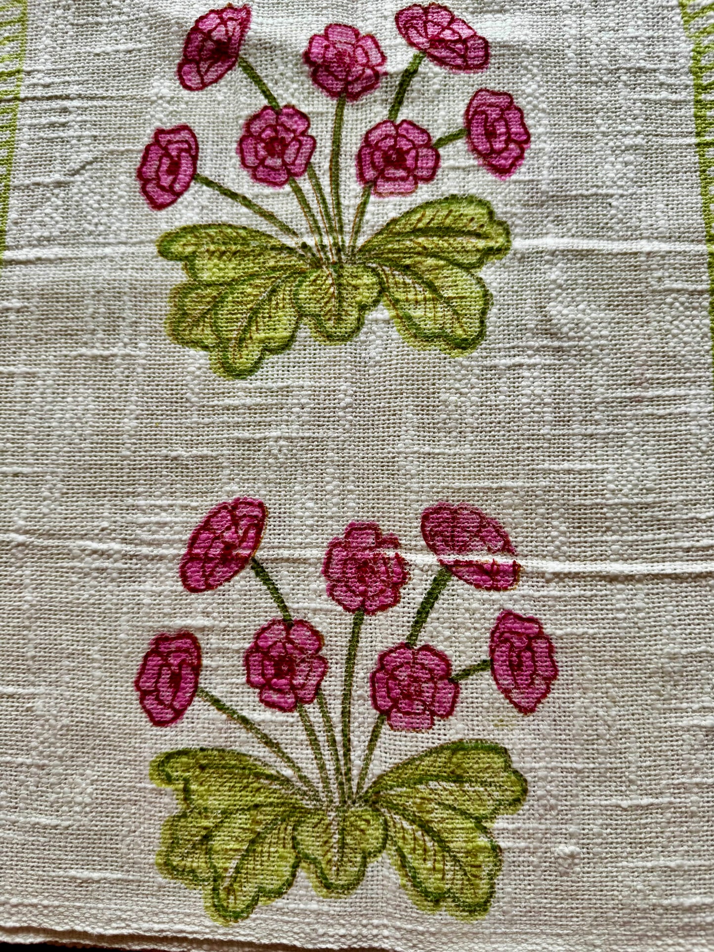 Close up of hand block printed placemats of pink flowers and green leaves on a textured fabric background