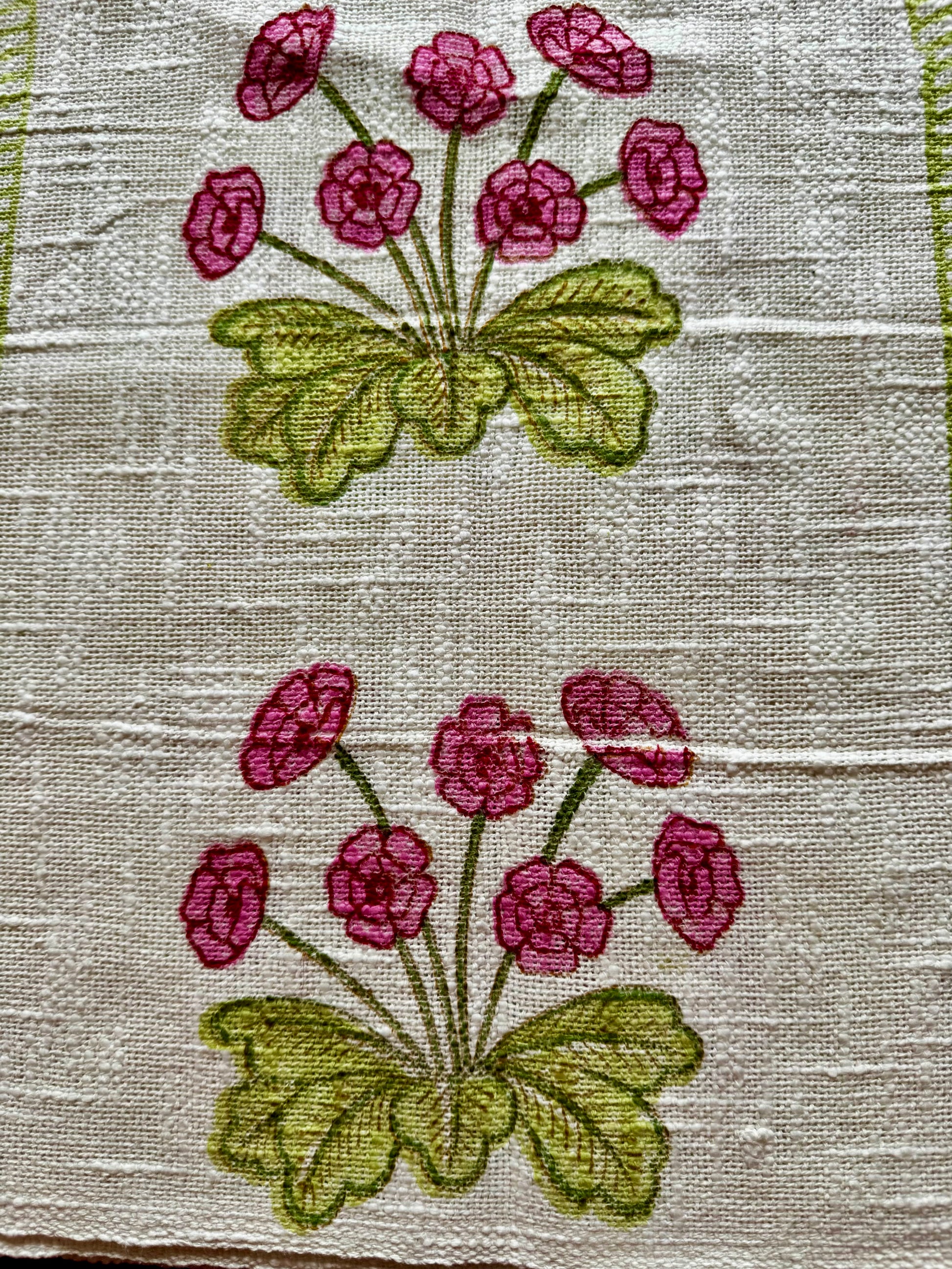 Close up of hand block printed placemats of pink flowers and green leaves on a textured fabric background