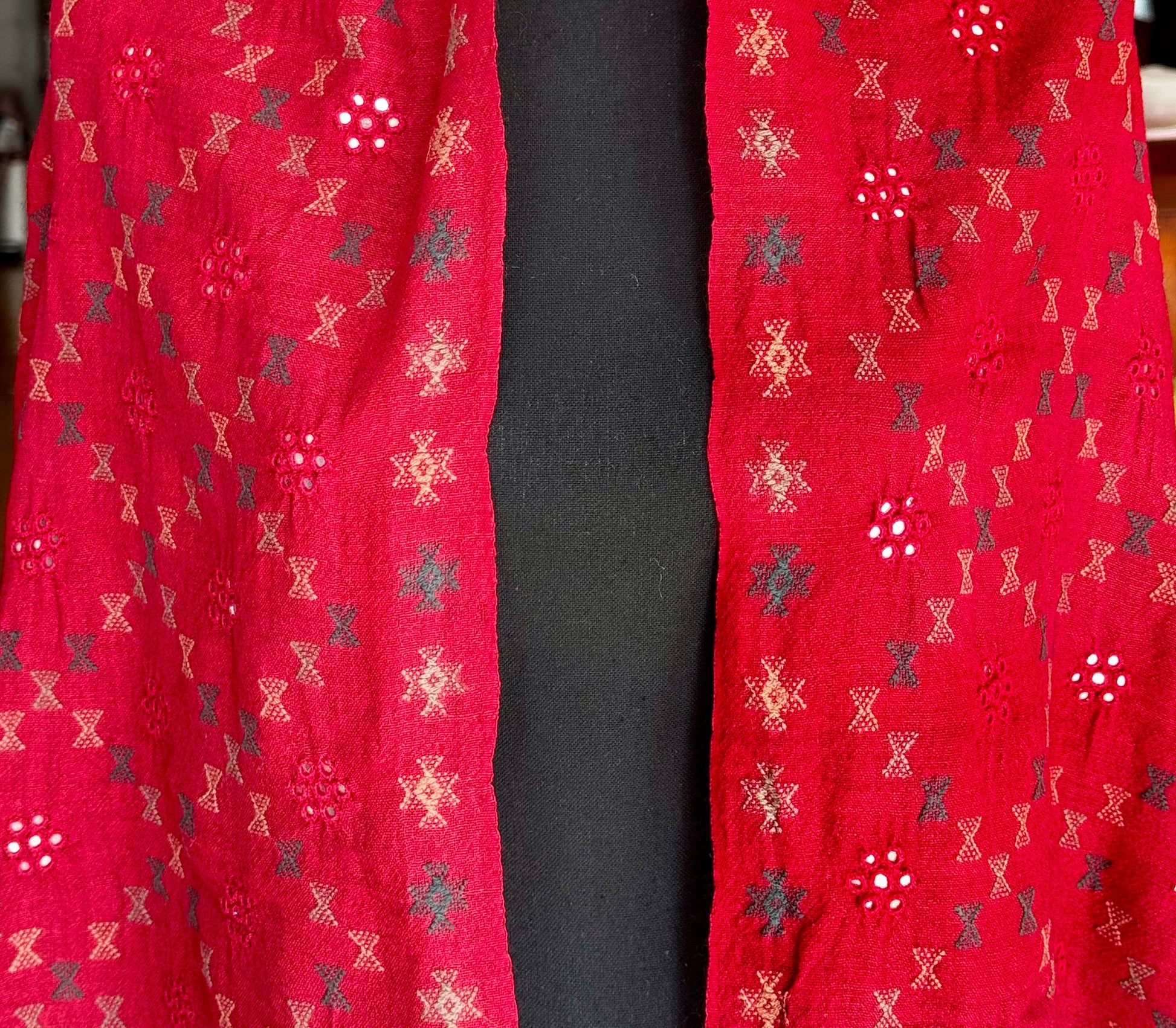 Red stole with geometric pattern Soof style embroidery draped over a black surface