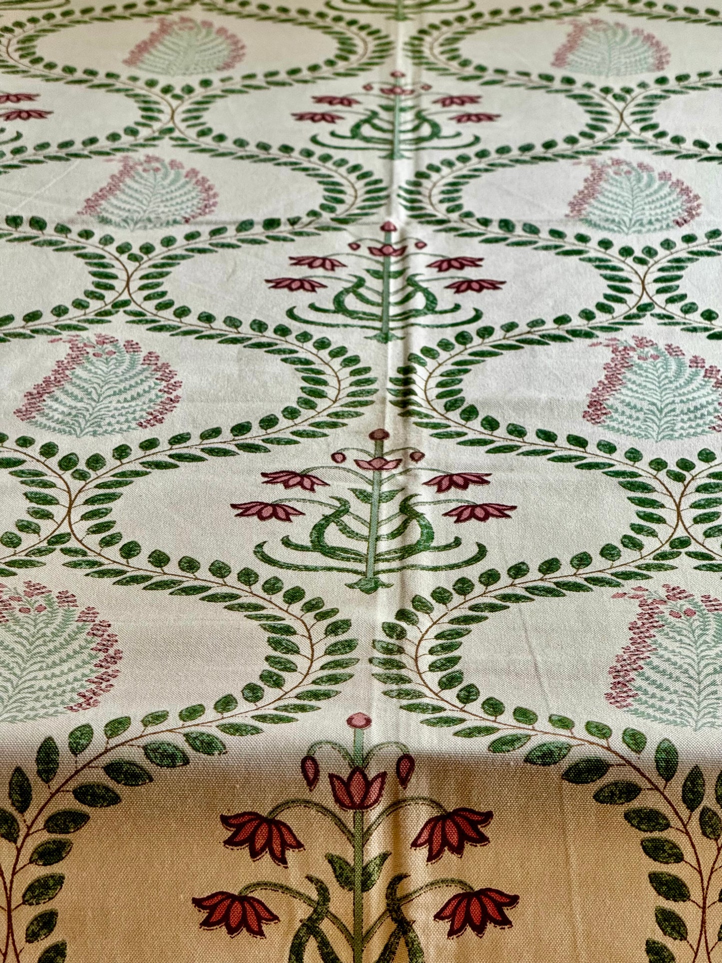 Close-up of a fabric with intricate floral and leaf patterns hand block printed tablecloth in green, red, and beige.
