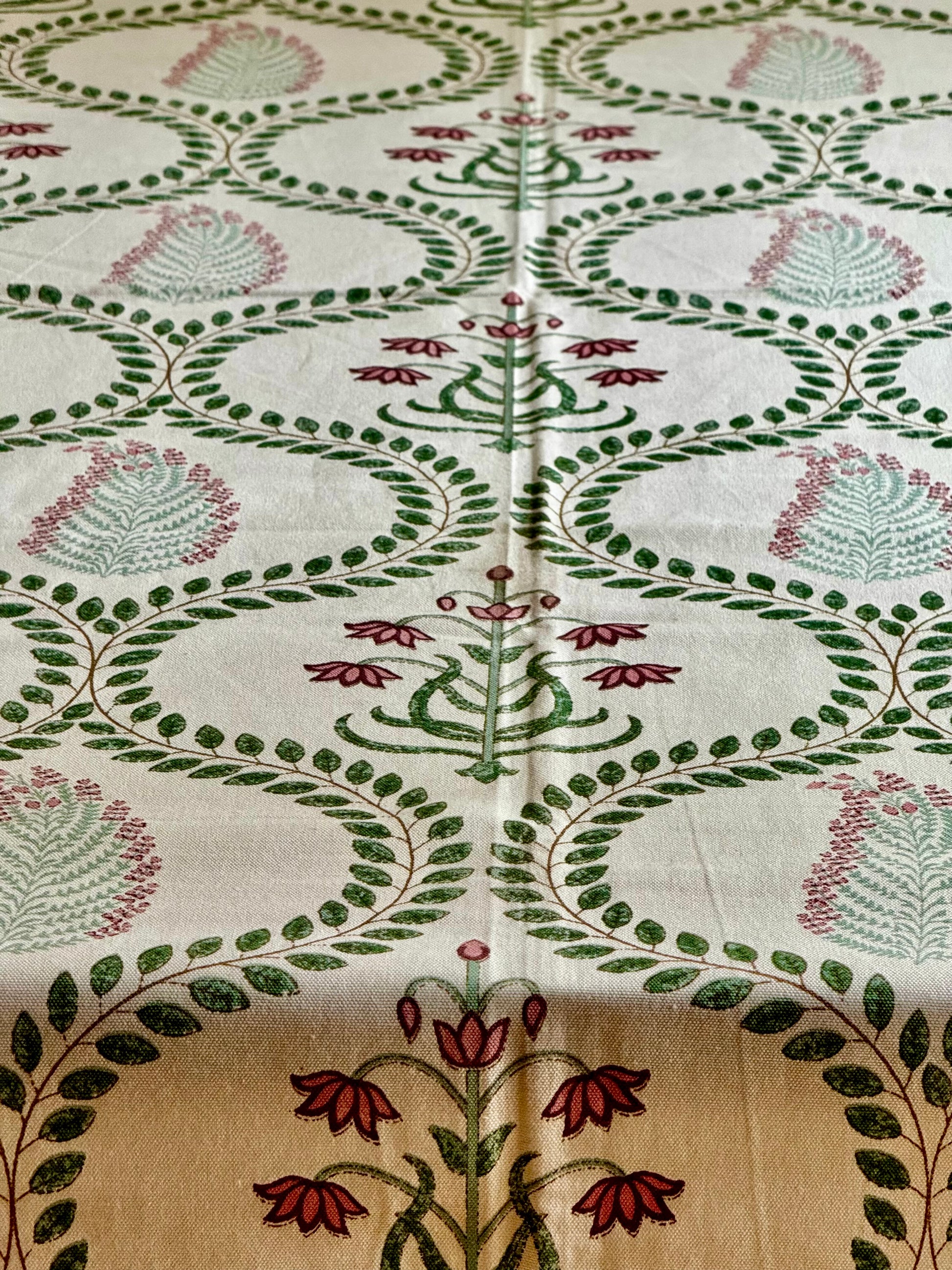 Close-up of a fabric with intricate floral and leaf patterns hand block printed tablecloth in green, red, and beige.