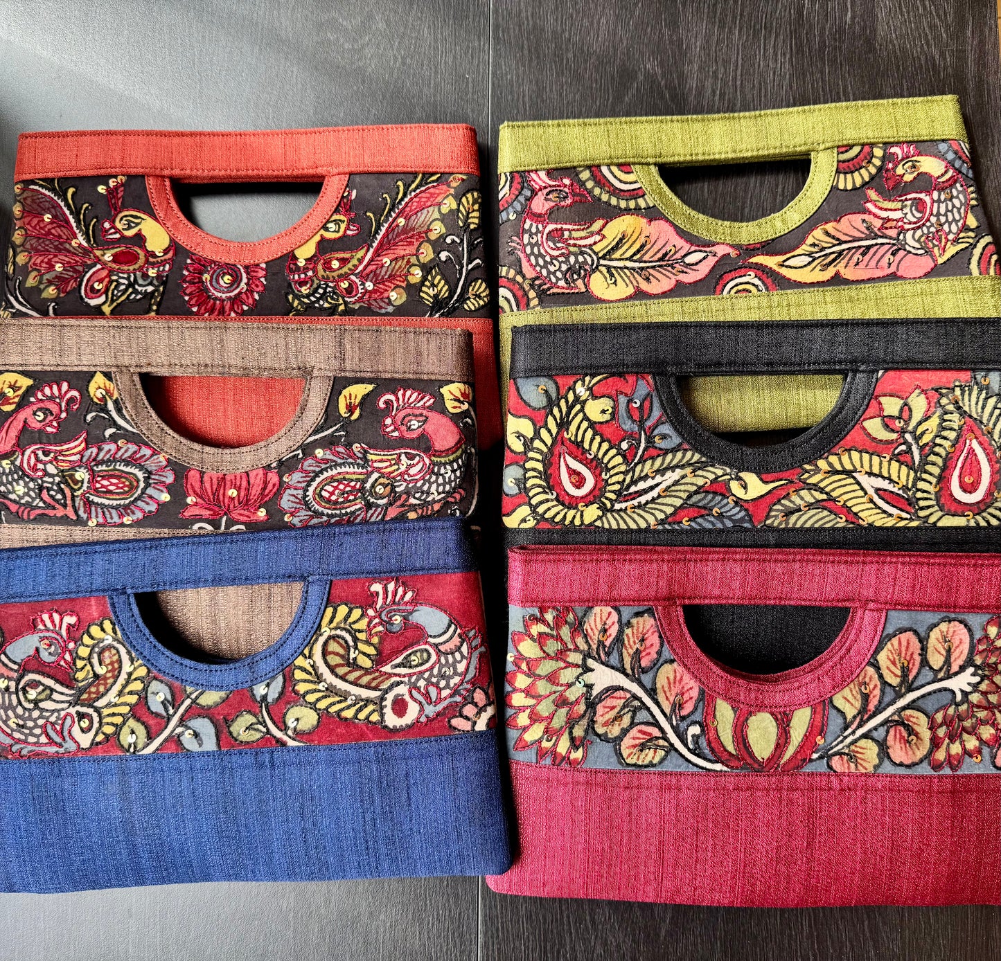 Collection of hand painted authentic Kalamkari clutches on black wood surface