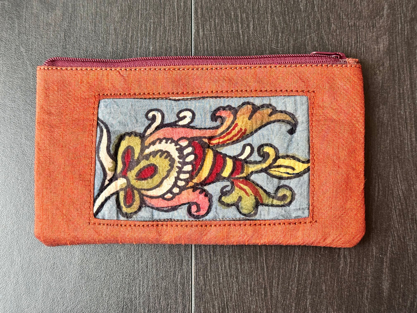 Close-up of a hand-painted makeup pouch with traditional Kalamkari art design featuring a bird and floral motifs in bright colors on a yellow background.