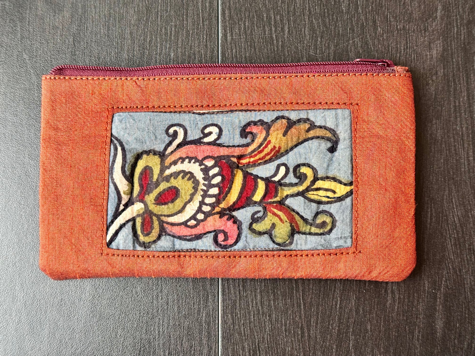 Close-up of a hand-painted makeup pouch with traditional Kalamkari art design featuring a bird and floral motifs in bright colors on a yellow background.