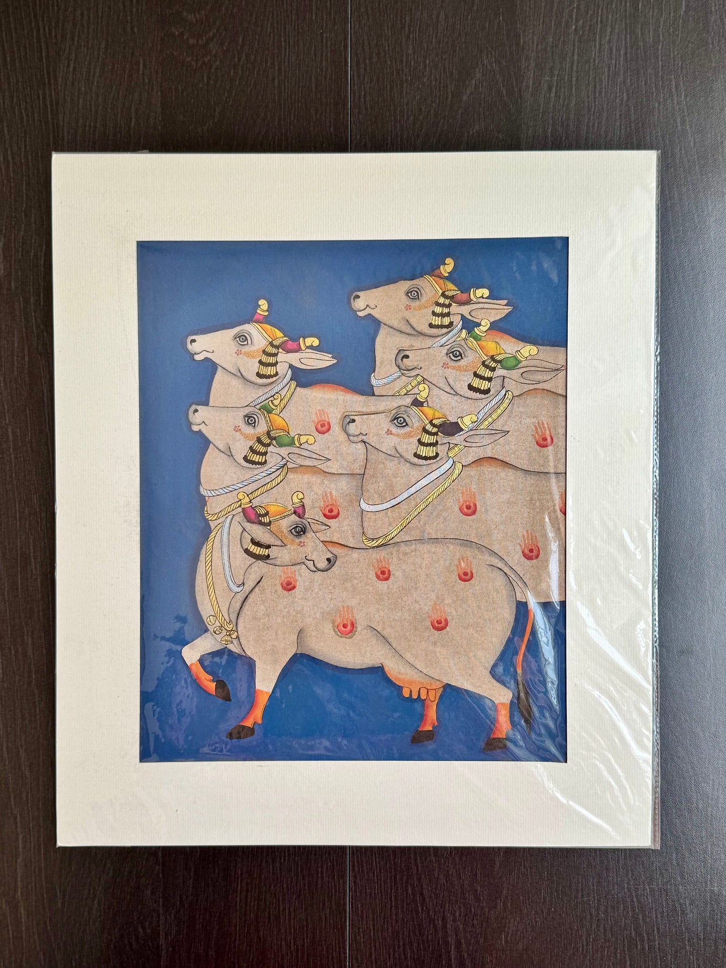 Pichwai Art paintings of four decorated cows on a blue background, framed in white.