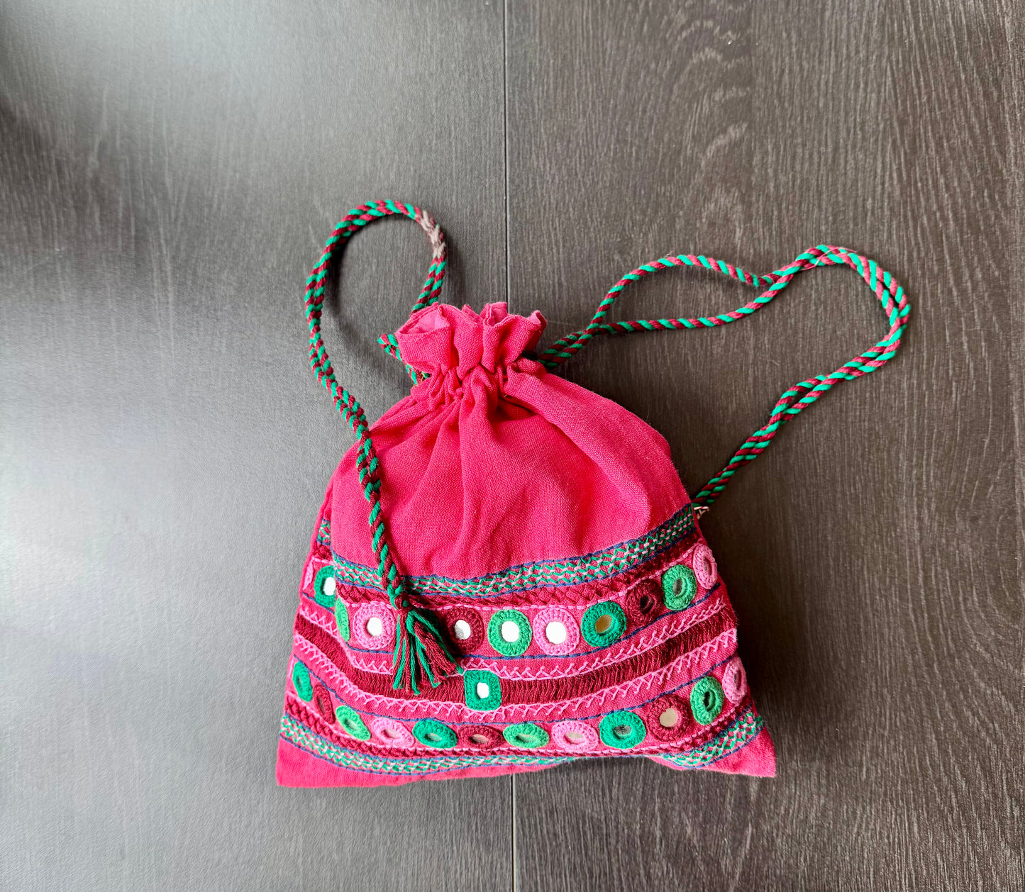 A traditional Lambani embroidery art potli bag with red, green, and beige colors, featuring geometric patterns and a drawstring closure.