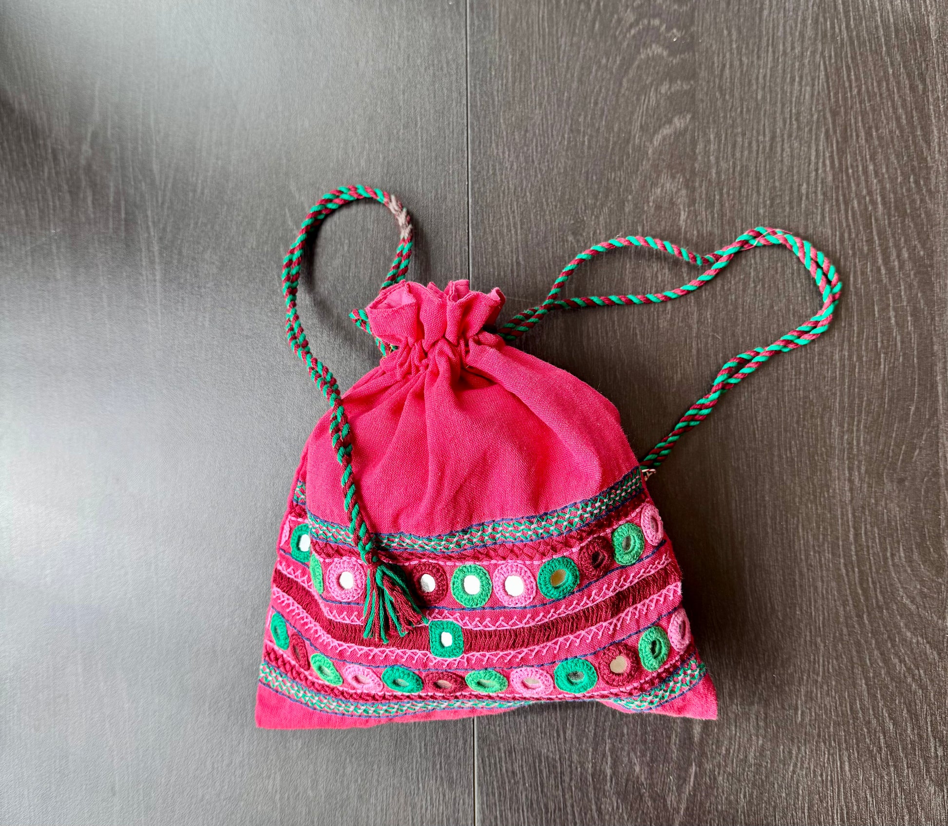 A traditional Lambani embroidery art potli bag with red, green, and beige colors, featuring geometric patterns and a drawstring closure.