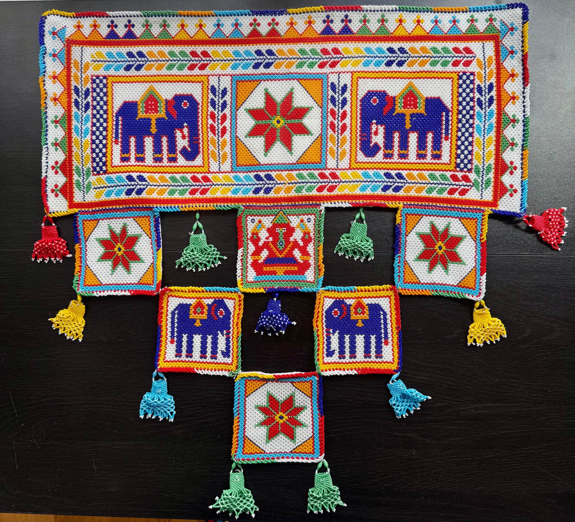 Colorful Motikaam wall hanging with patterns and tassels on a dark background