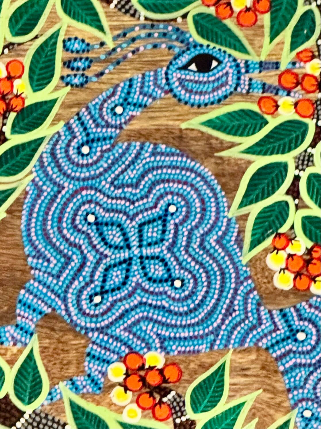 Details of Bhil artwork of a snake with leaves and berries on a wooden background