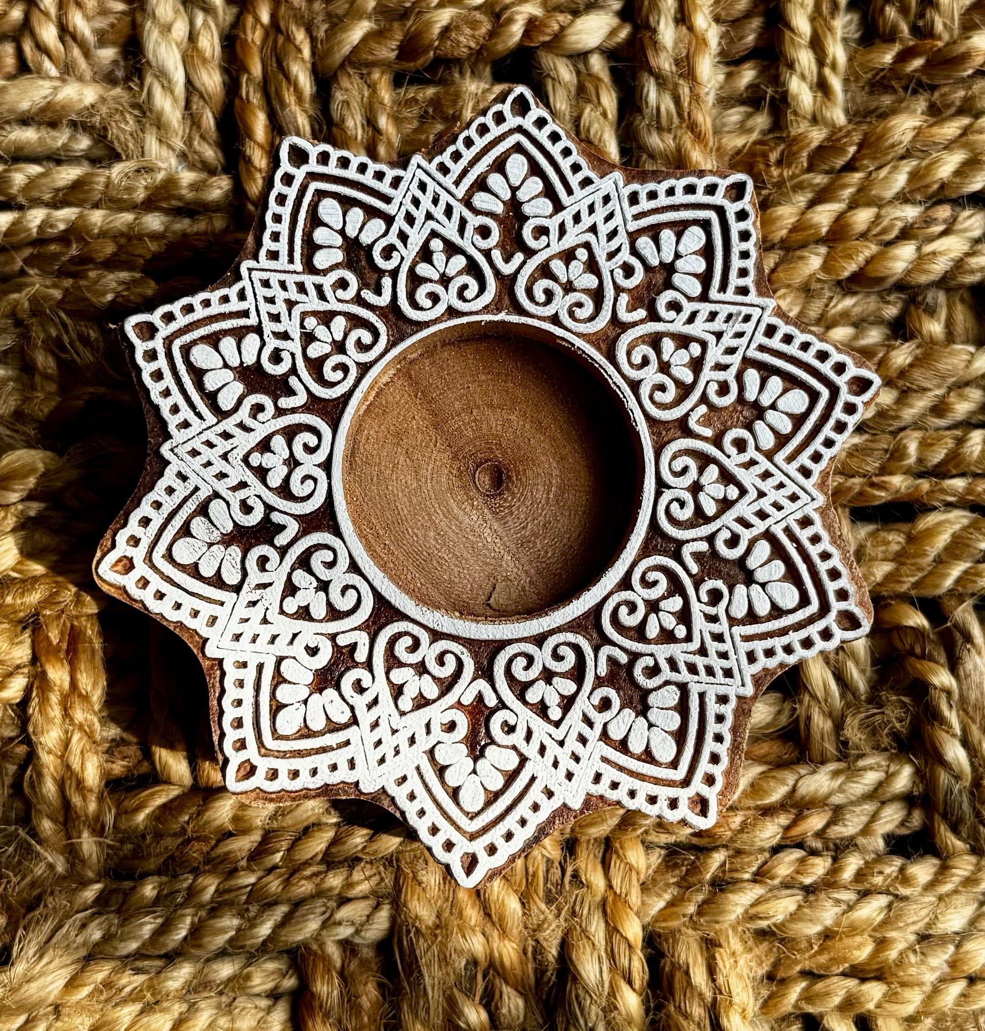 Decorative hand engraved wooden block candle holder with intricate patterns on a woven background