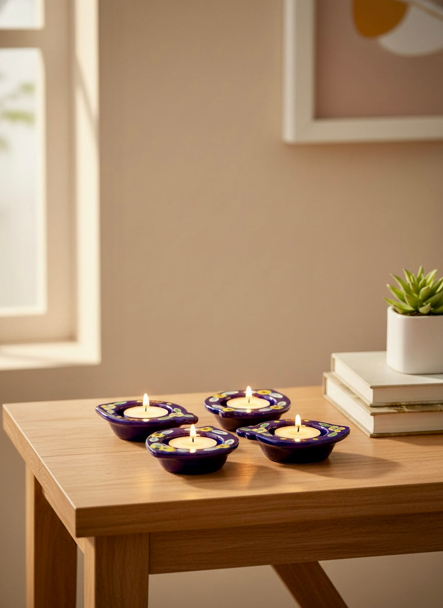 Four purple Jaipur Blue pottery candle holders with candles on a wooden table near a window.
