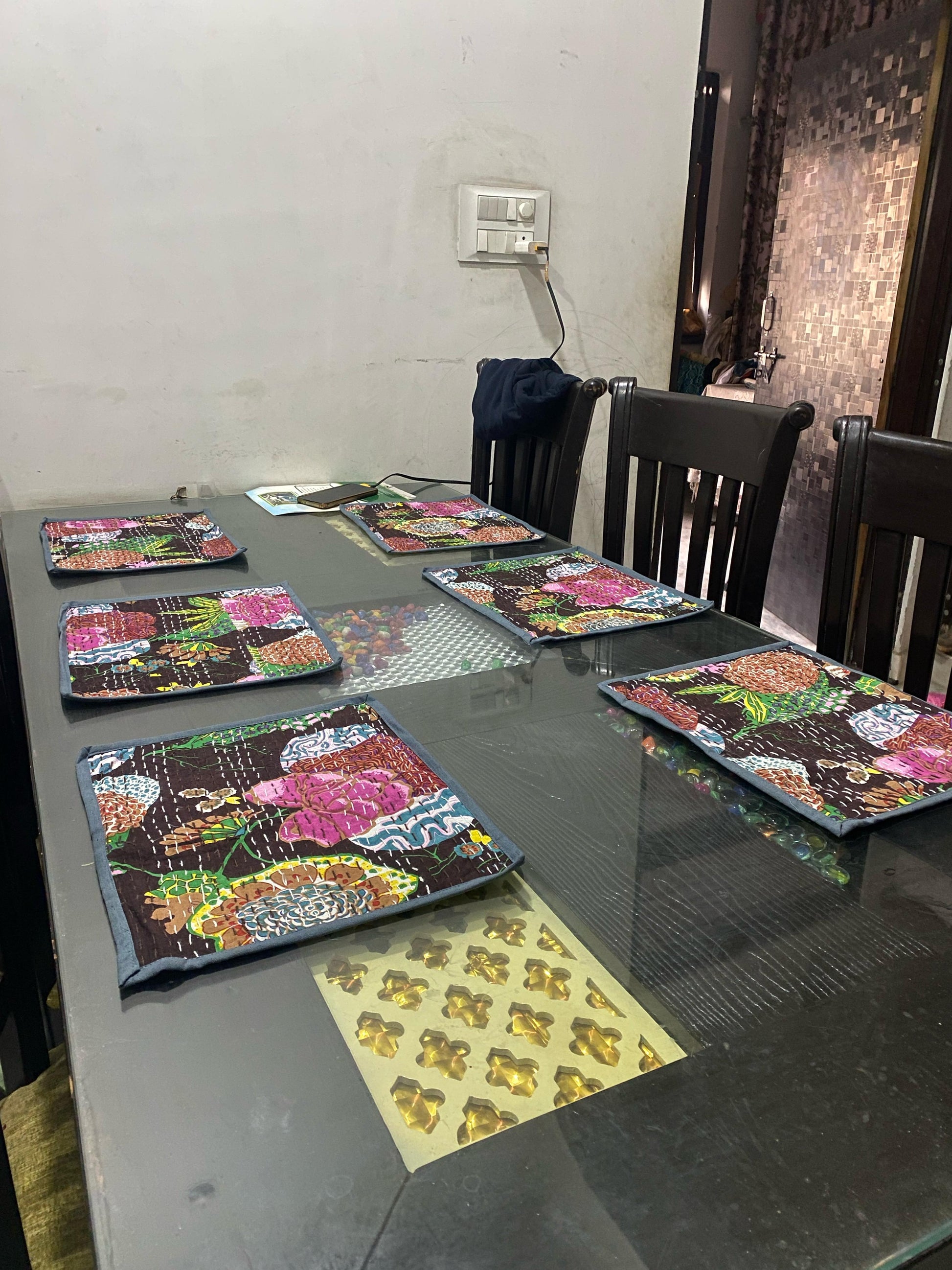 Dining table with colorful gray Kantha work reversible placemats and a puzzle on a glass table.