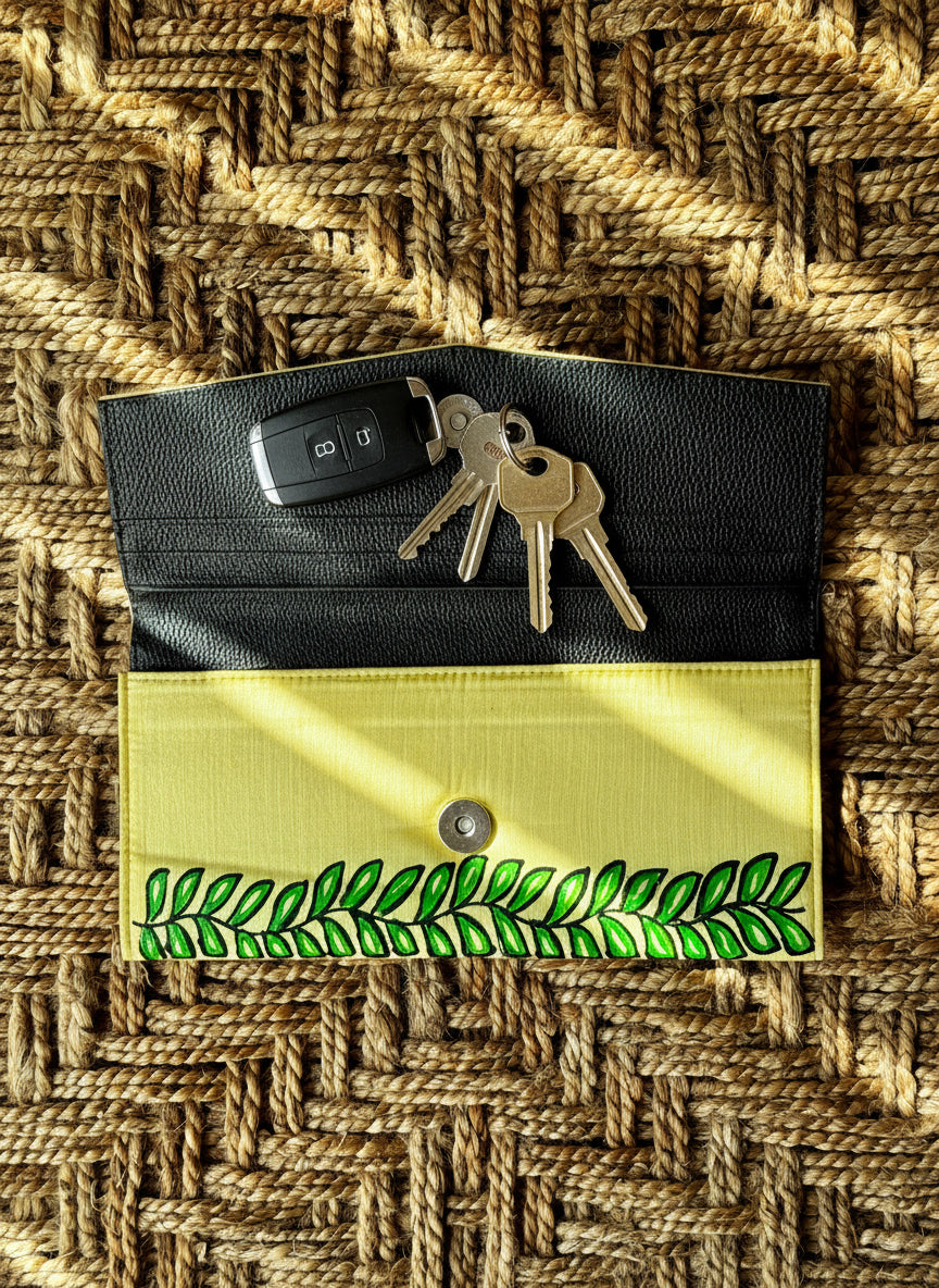 Black and yellow clutch bag with green Madhubani hand painted leaf design on a woven background