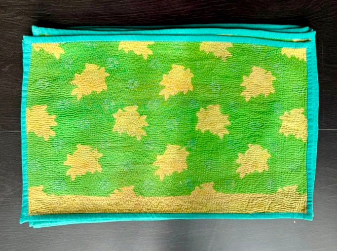 Green Kantha work placemats with yellow floral patterns on a dark surface