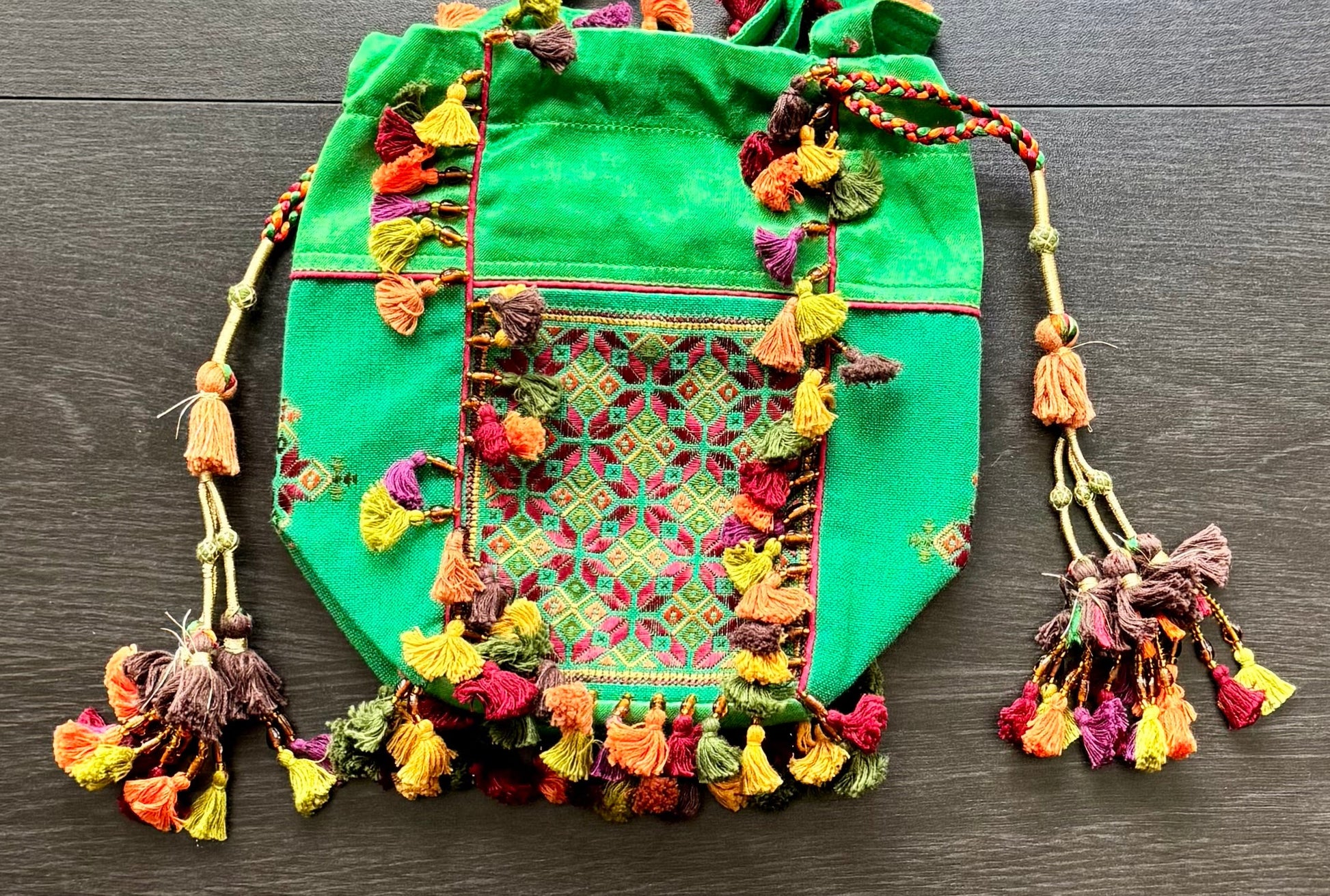 Green Kutchi Soof work embroidered bag with colorful tassels on a wooden surface