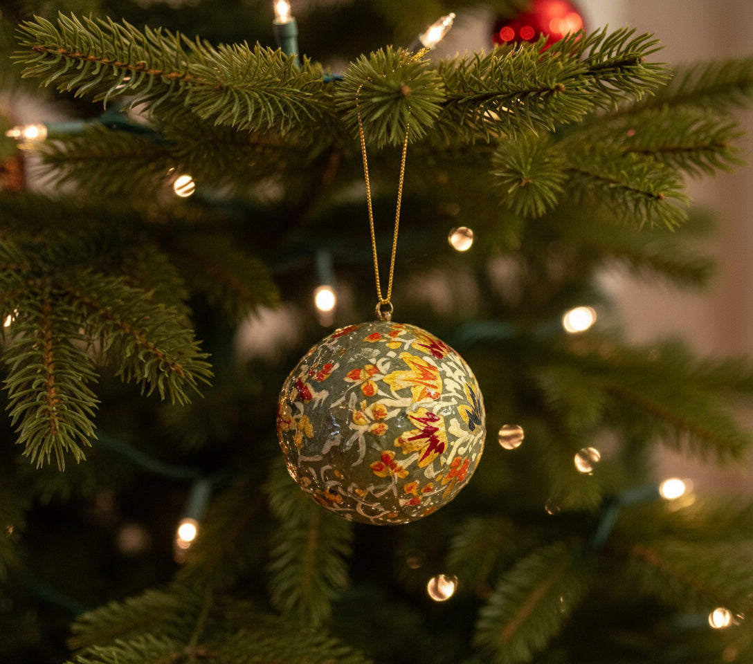 Decorative spherical ornament with floral pattern hanging by a hand against a neutral background