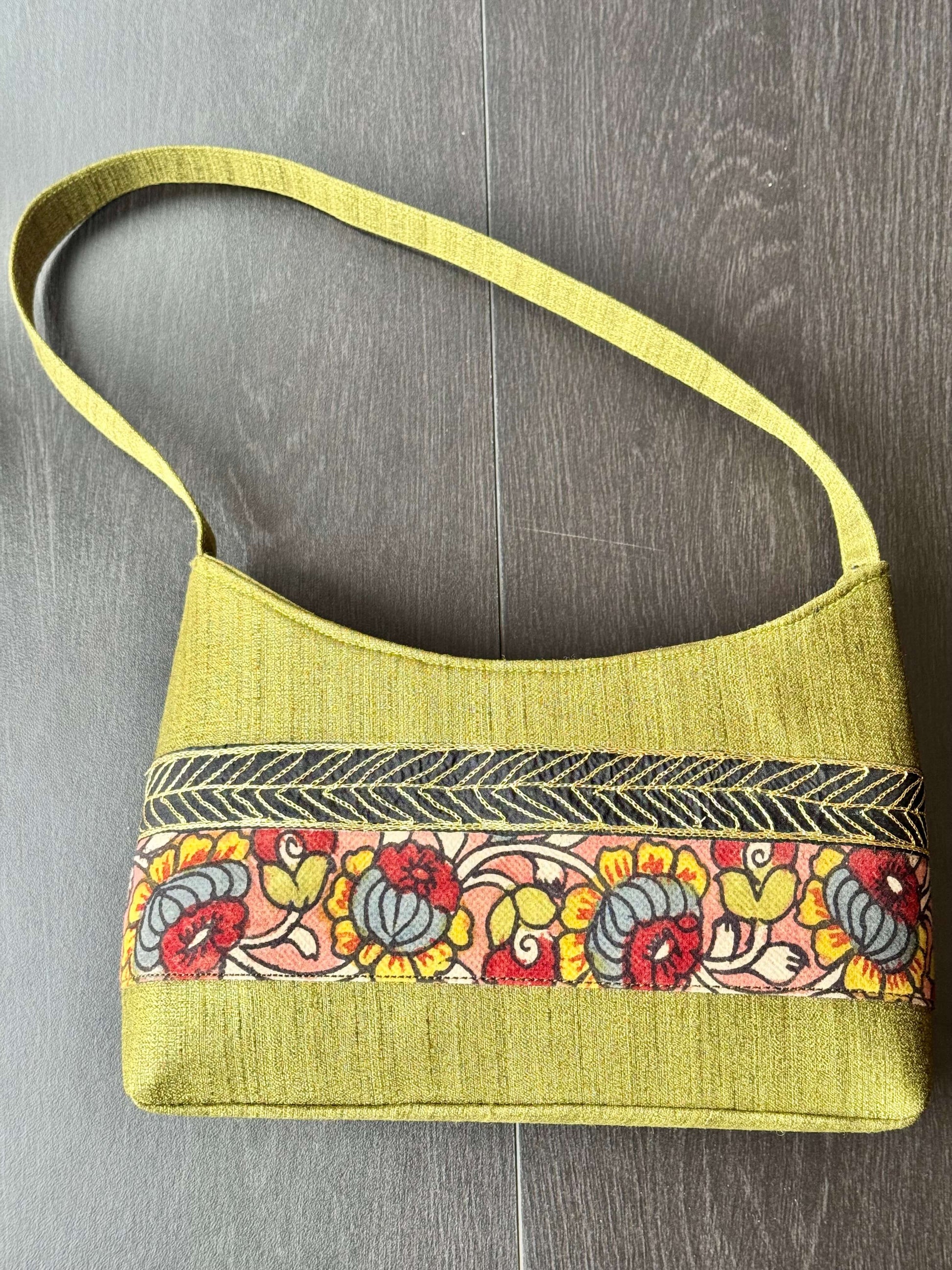 Green handbag with a colorful floral hand painted Kalamkari pattern on a wooden surface