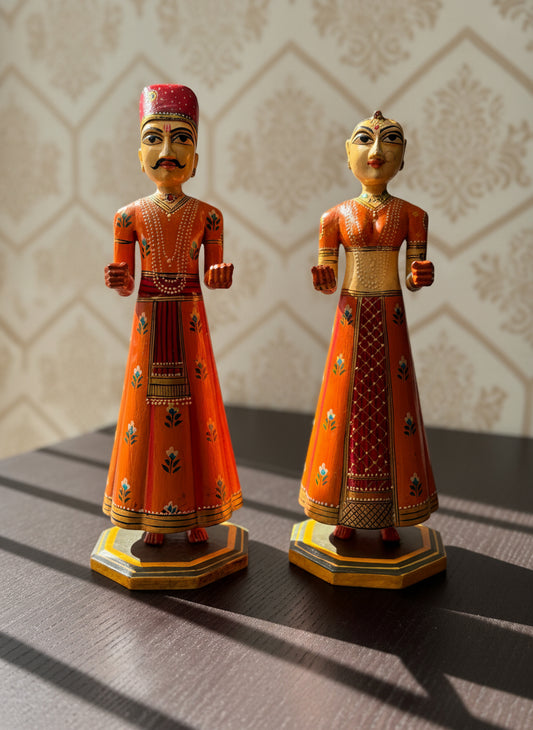 Two ornate wood figurines in traditional attire on a textured surface.