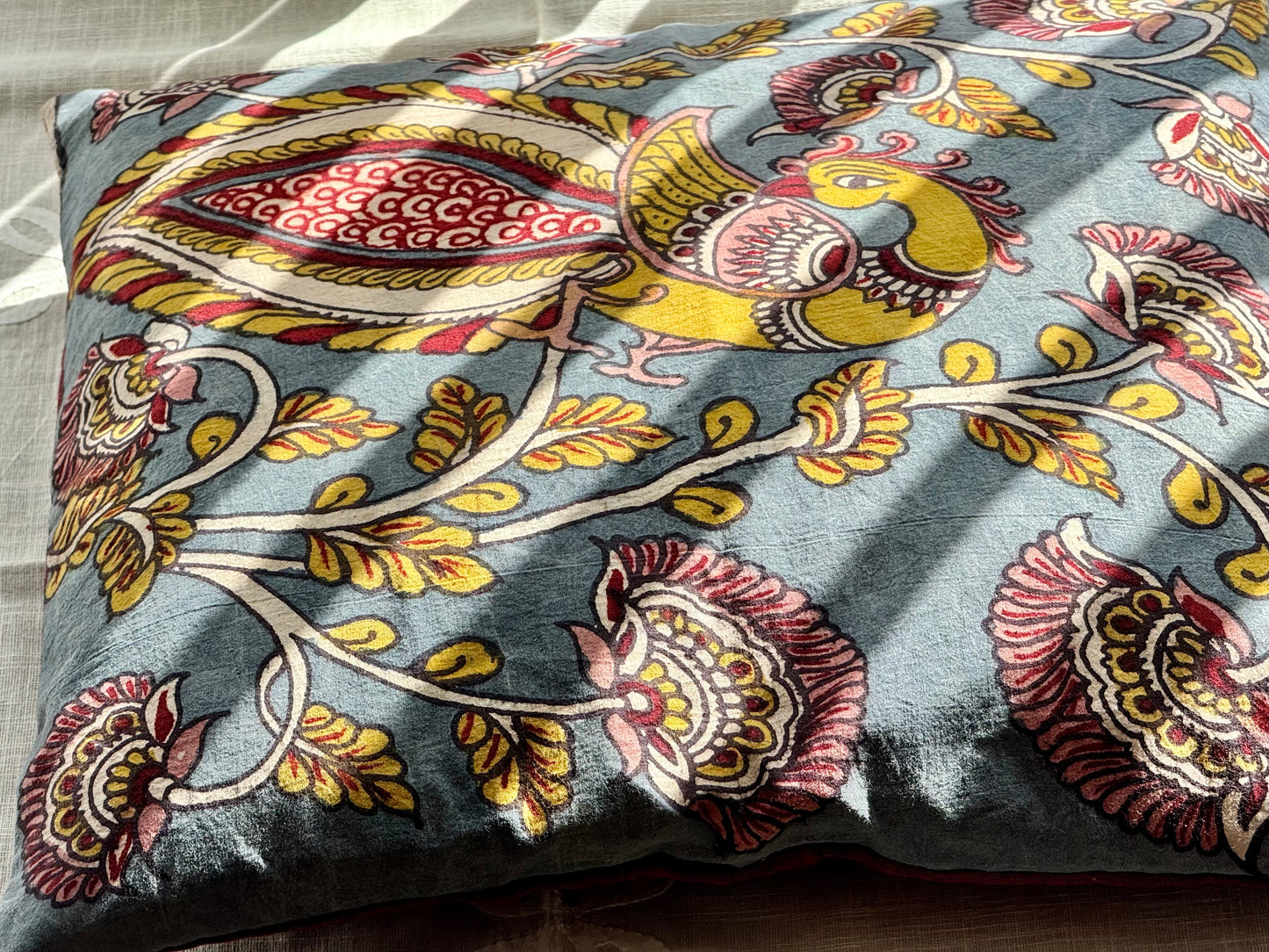 A set of artisanal Kalamkari hand-painted cushion covers with vibrant and intricate patterns laid out on a surface.