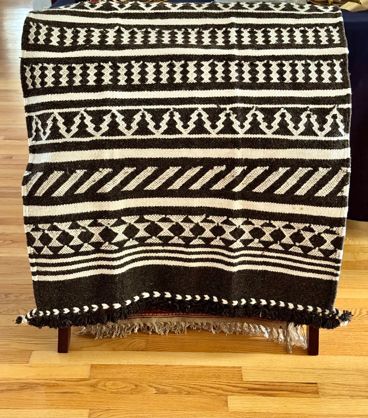 Black and white patterned Kutchi Kharad rug draped over a rack on a wooden floor