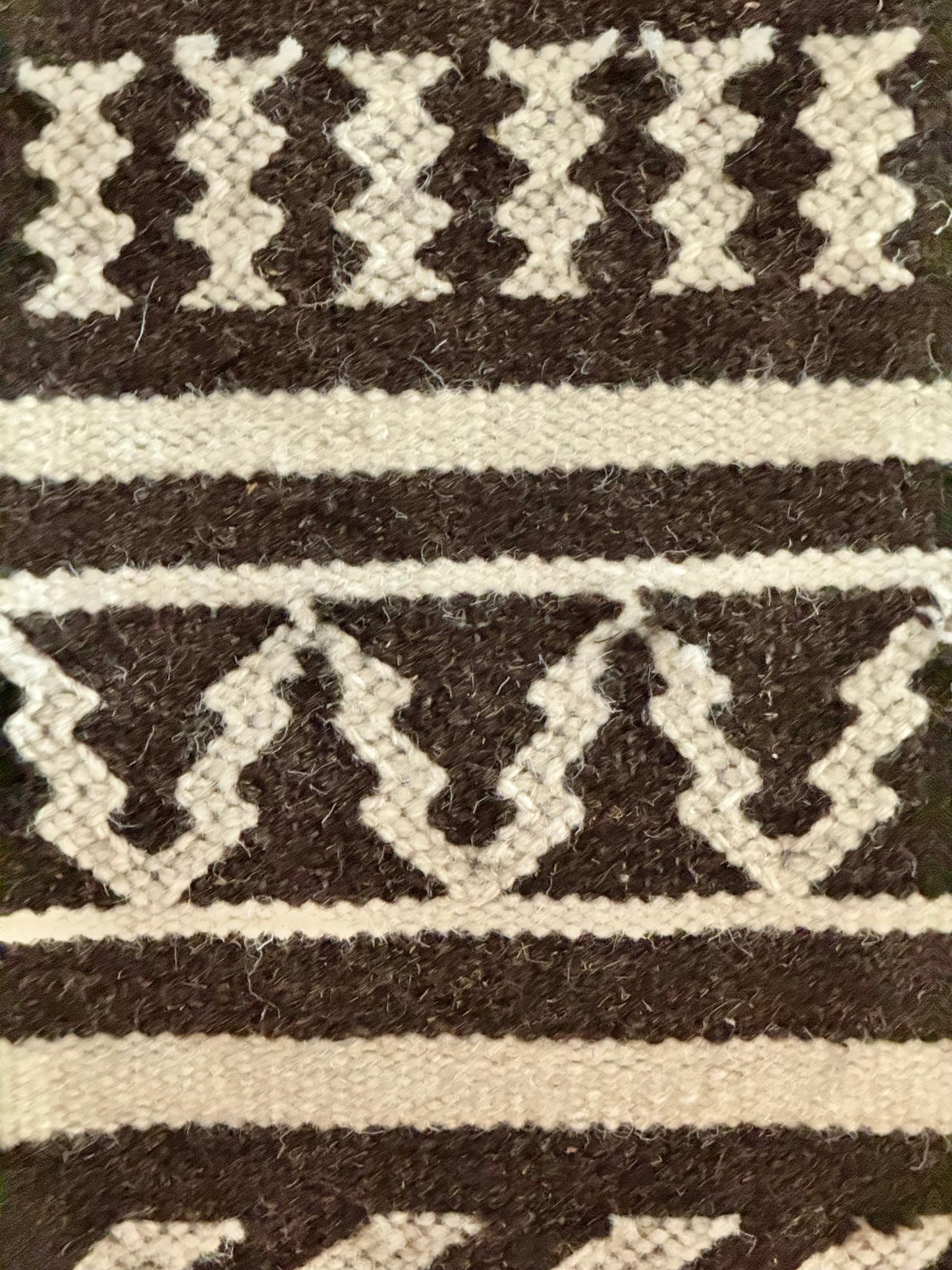 Close-up of a woven pattern Kutchi Kharad rug with black and white stripes on a textured background