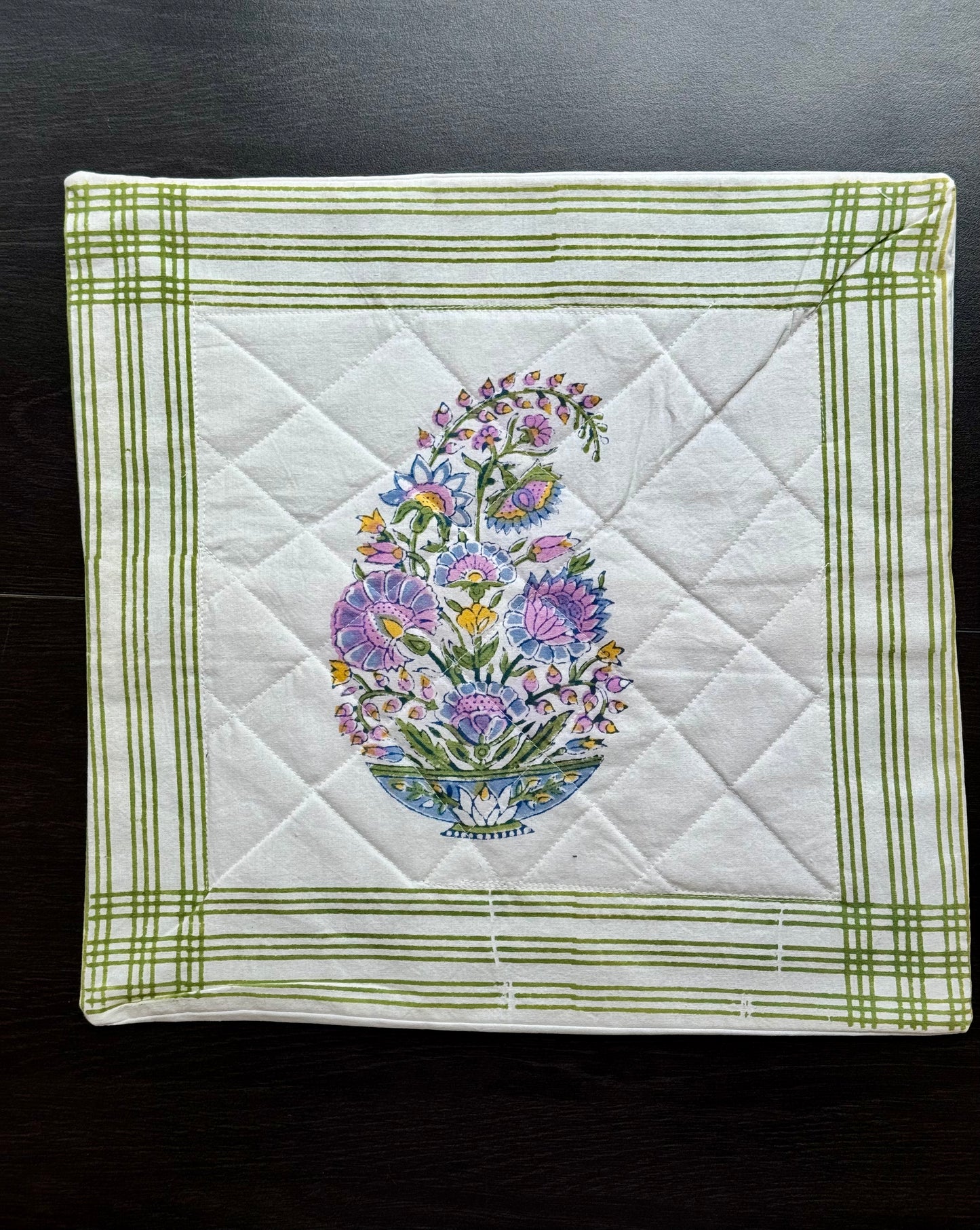 Quilted square cushion cover with floral hand block printed design in the center on a dark background