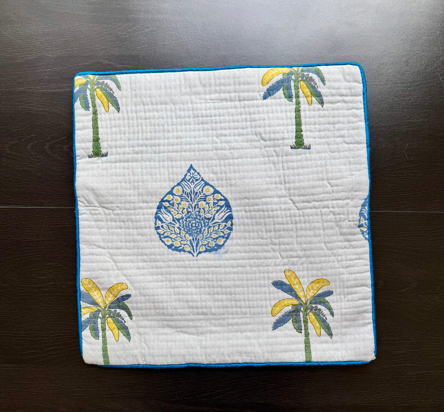 Quilted hand block printed cushion cover with palm tree and floral pattern on a dark surface