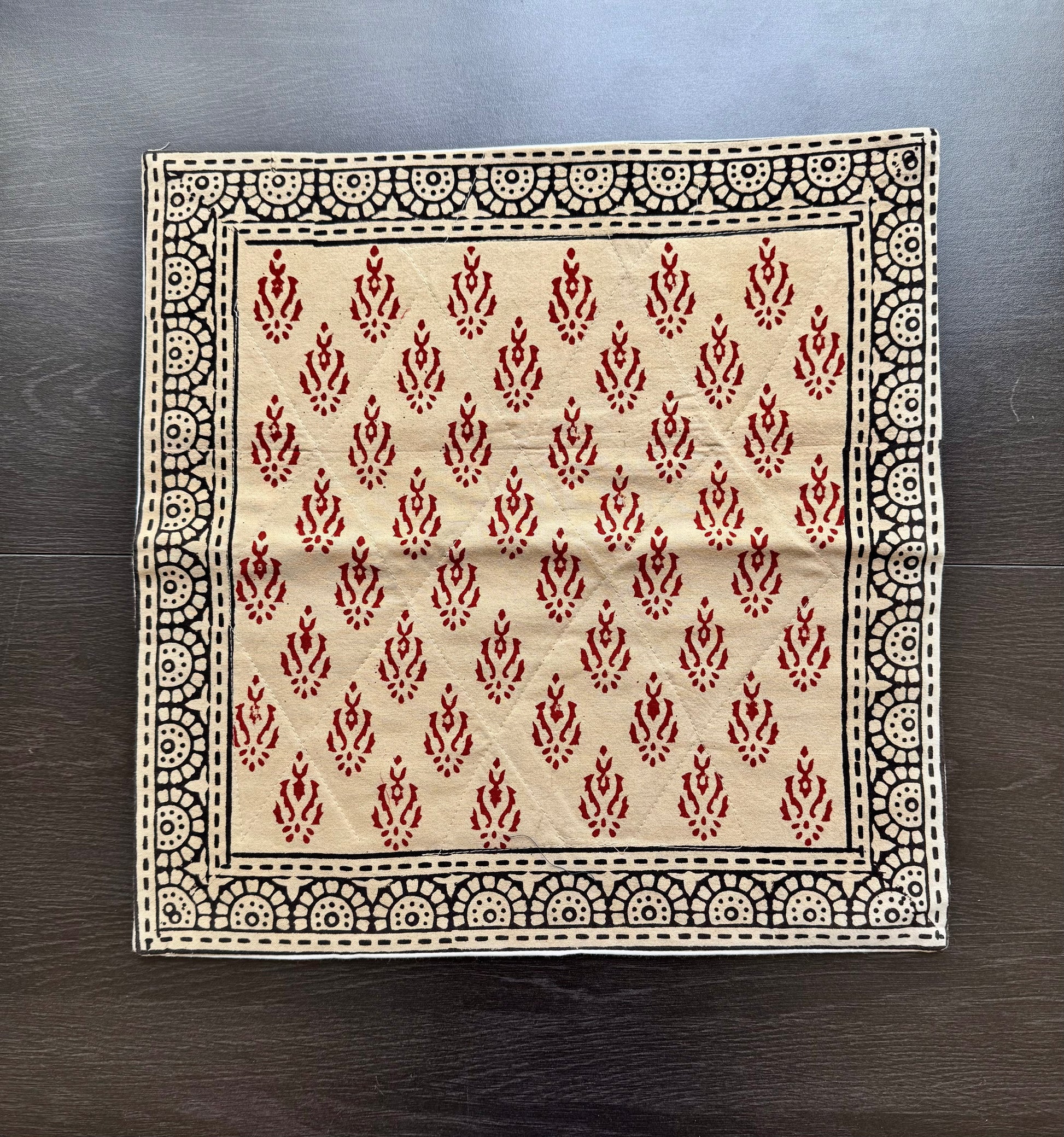 Beige fabric cushion cover in Bagru hand block print with red and black pattern on a wooden surface