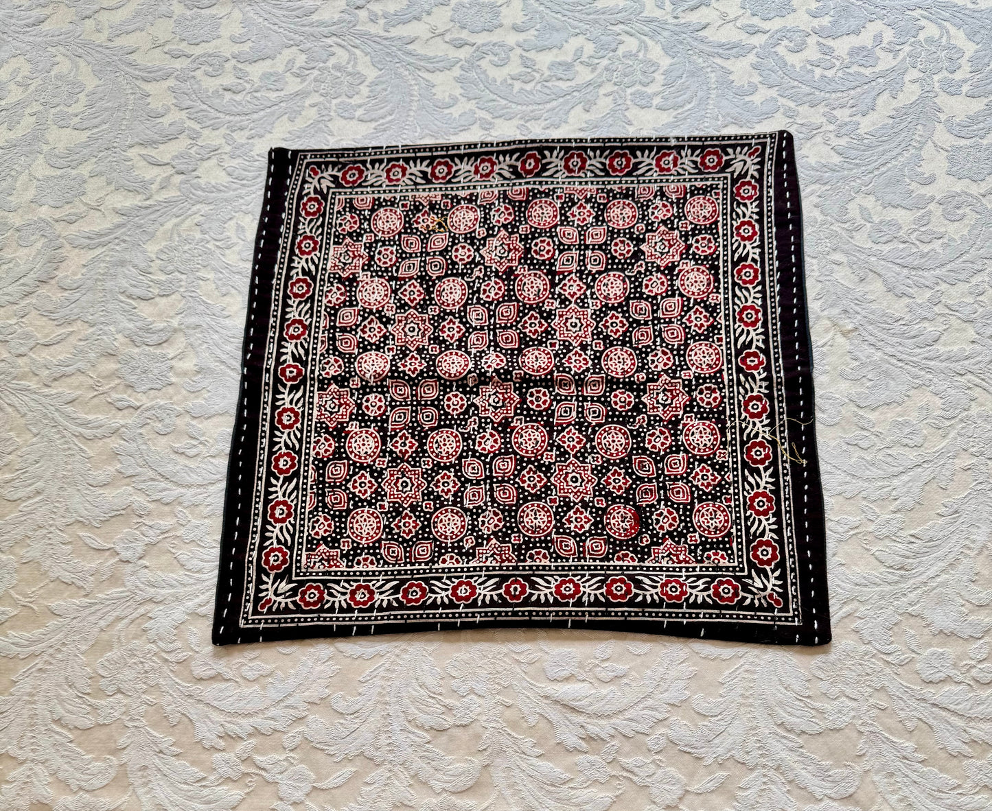 Decorative black and red pillow in Ajrakh hand block print pattern on a textured white background