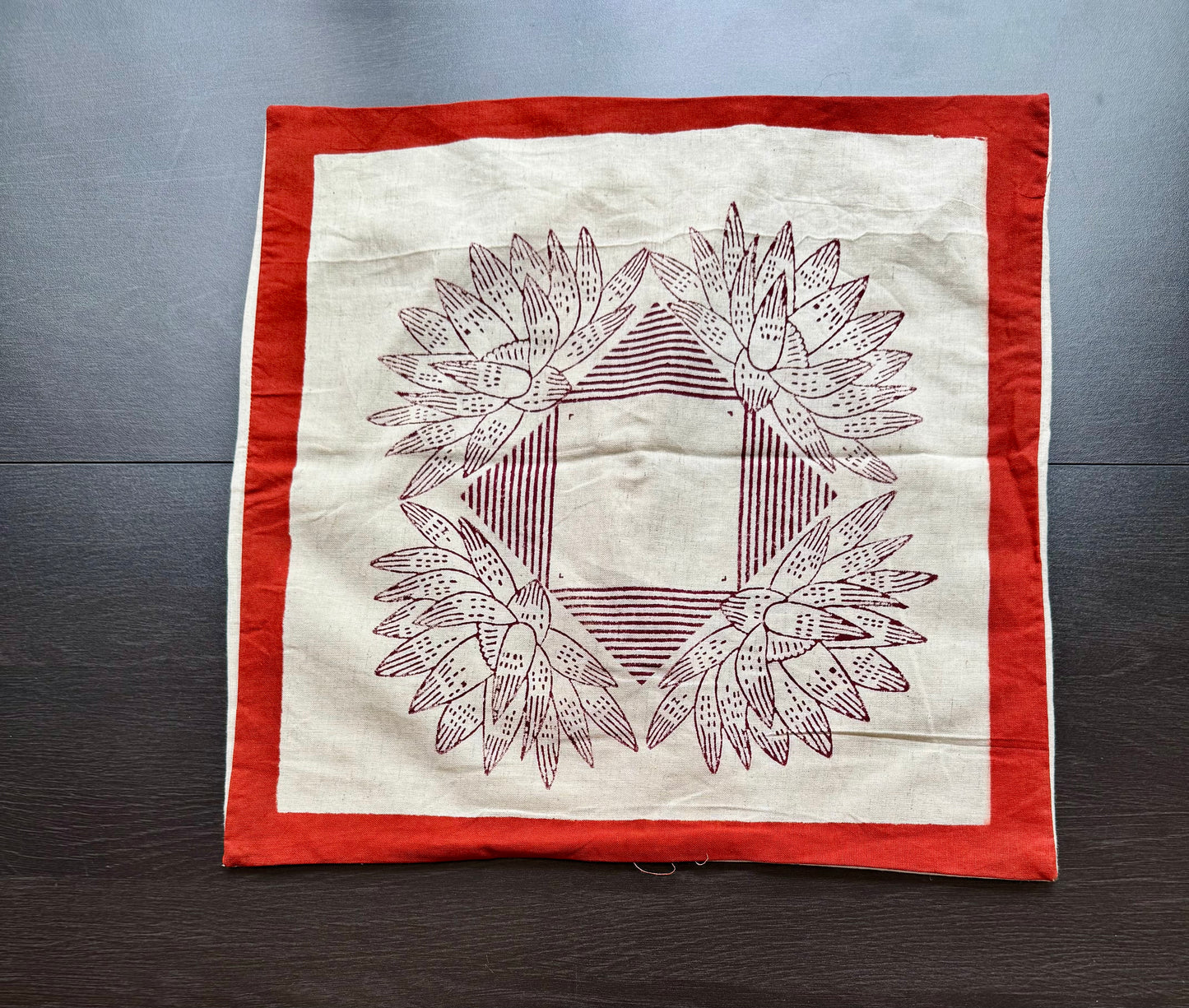 Hand block printed cushion cover with red border and geometric floral design on a wooden surface
