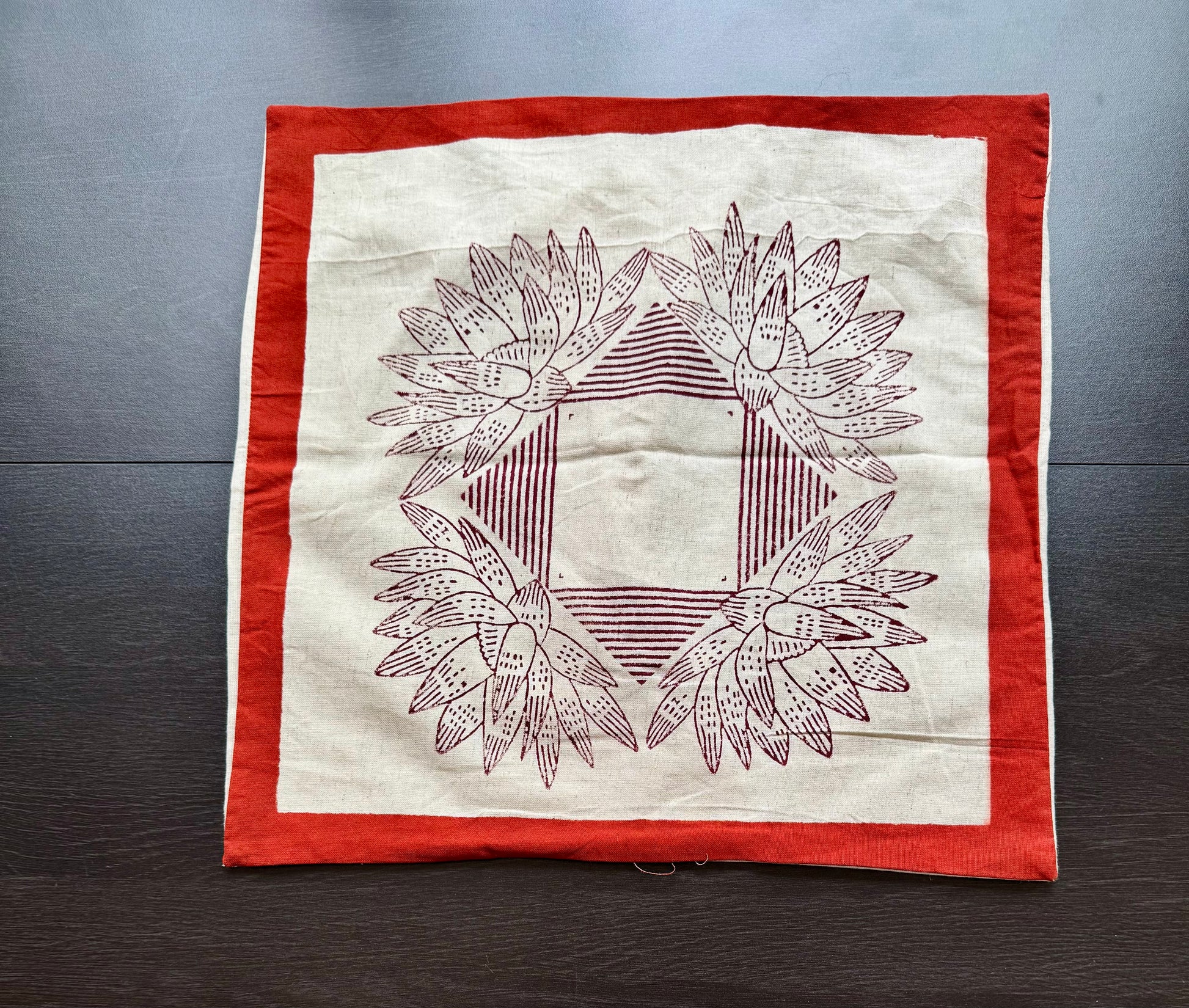 Hand block printed cushion cover with red border and geometric floral design on a wooden surface