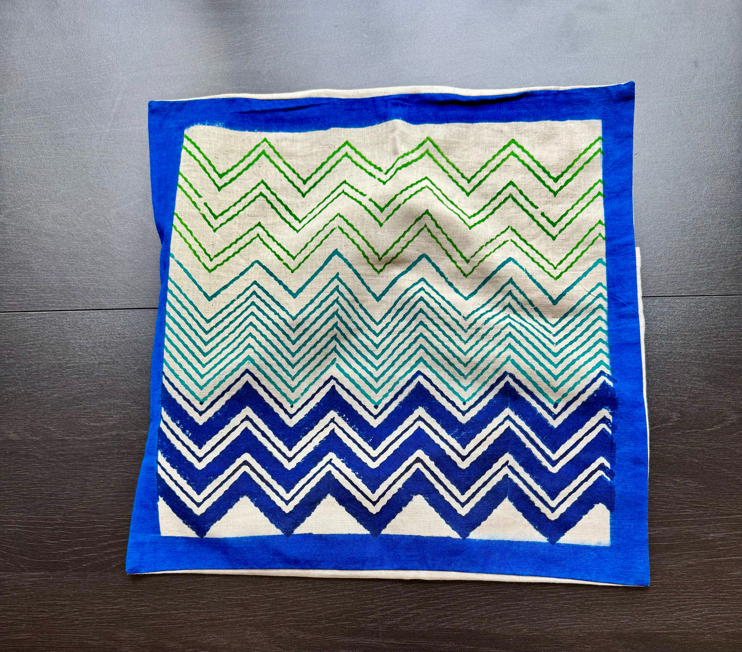 Hand block print cushion cover with blue, green, and white zigzag pattern on a wooden surface