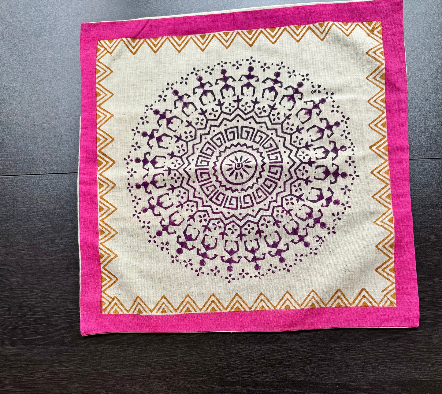 Warli style hand block print cushion cover against dark  background, bordered by pink and gold