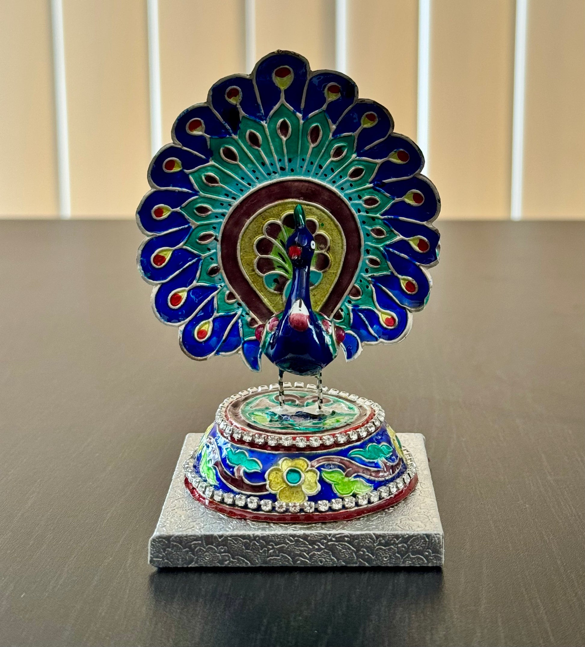 Decorative Gulabi Meenakari silver peacock sculpture on a gray surface with a neutral background
