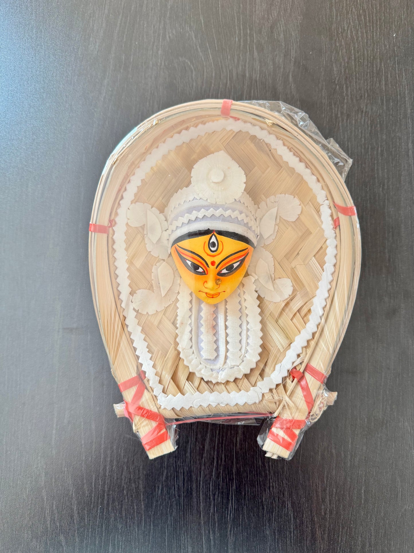 Decorative Sholapith Art face of Devi goddess in a woven frame on a dark surface