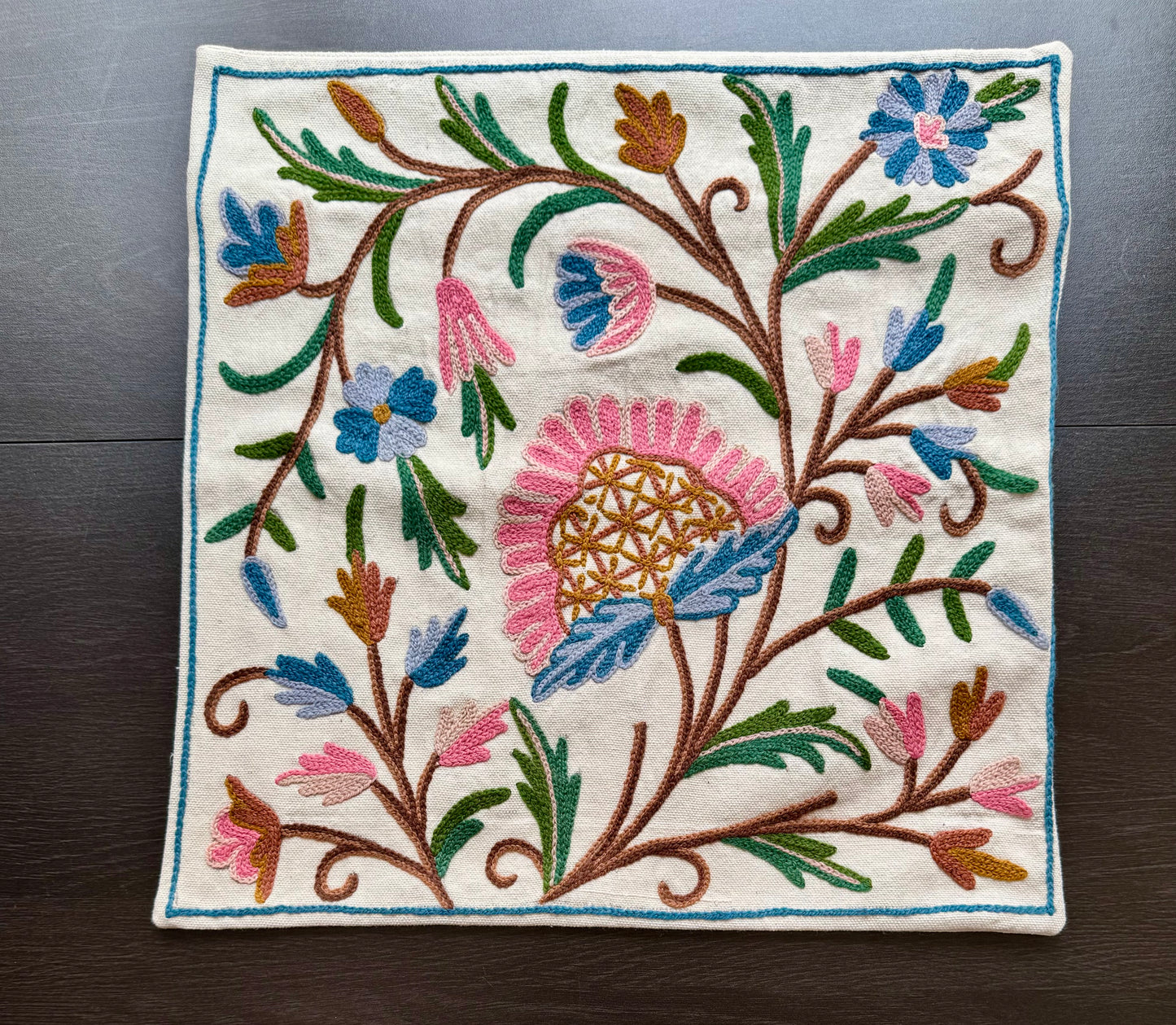 Embroidered cushion cover with colorful floral Kashmiri embroidery on a wooden surface