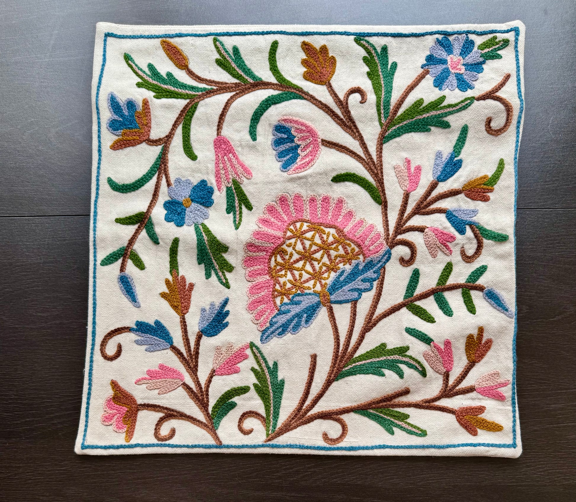 Embroidered cushion cover with colorful floral Kashmiri embroidery on a wooden surface