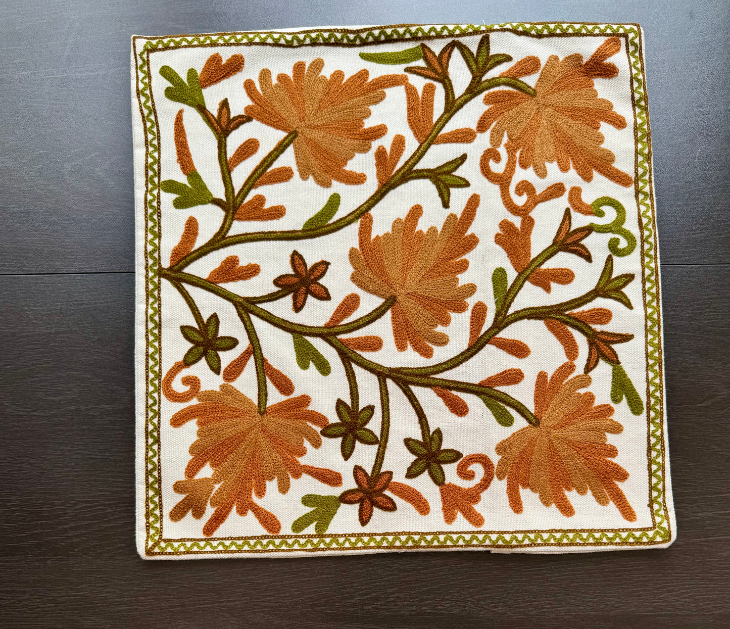 Embroidered square cushion cover with floral Kashmiri embroidery patterns on a wooden surface