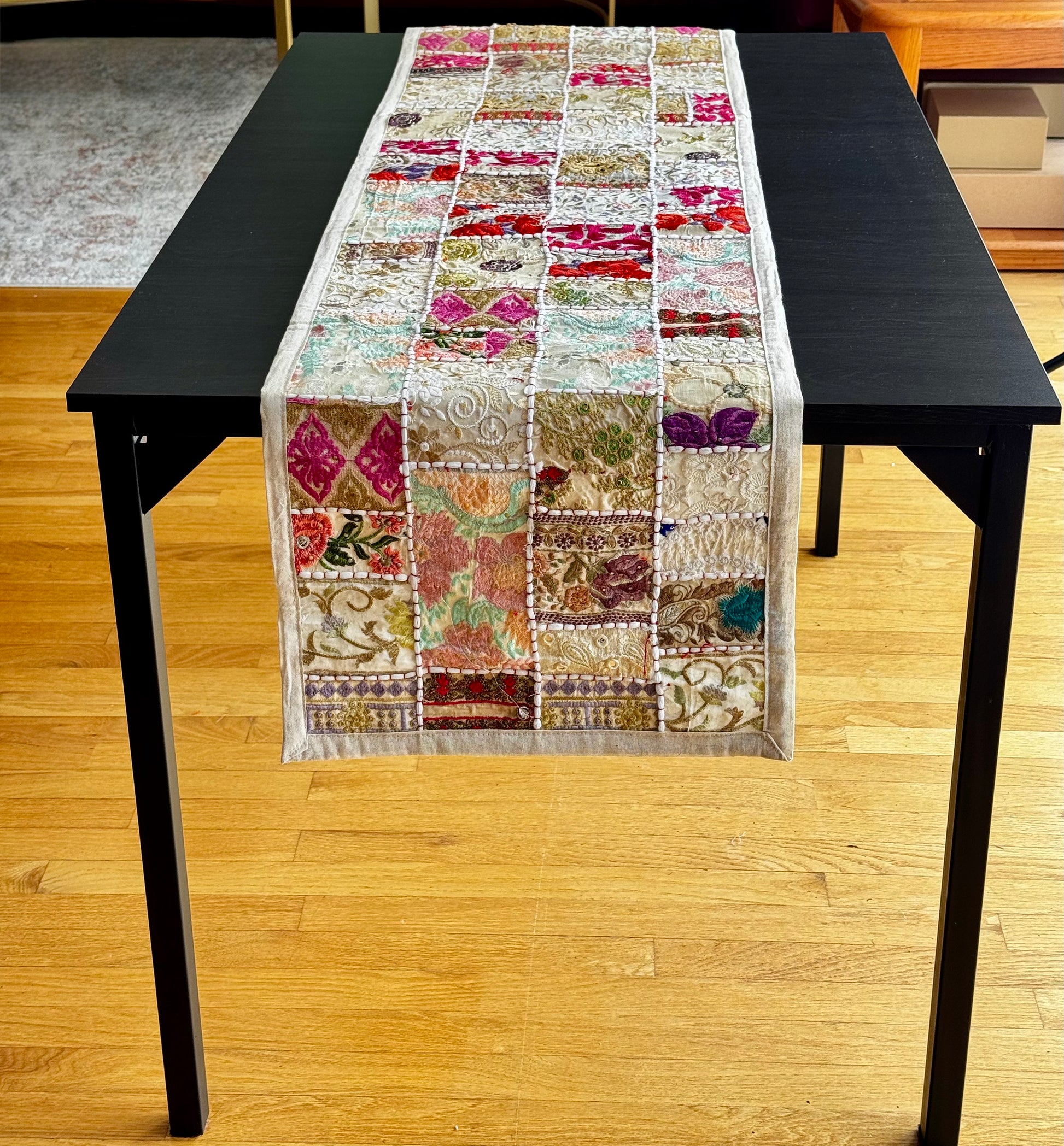Colorful Khambhadia patchwork table runner on a black table with a wooden floor background