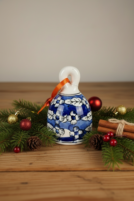 Decorative blue and white bell ornament with a red ribbon on a wooden surface with Christmas decorations.