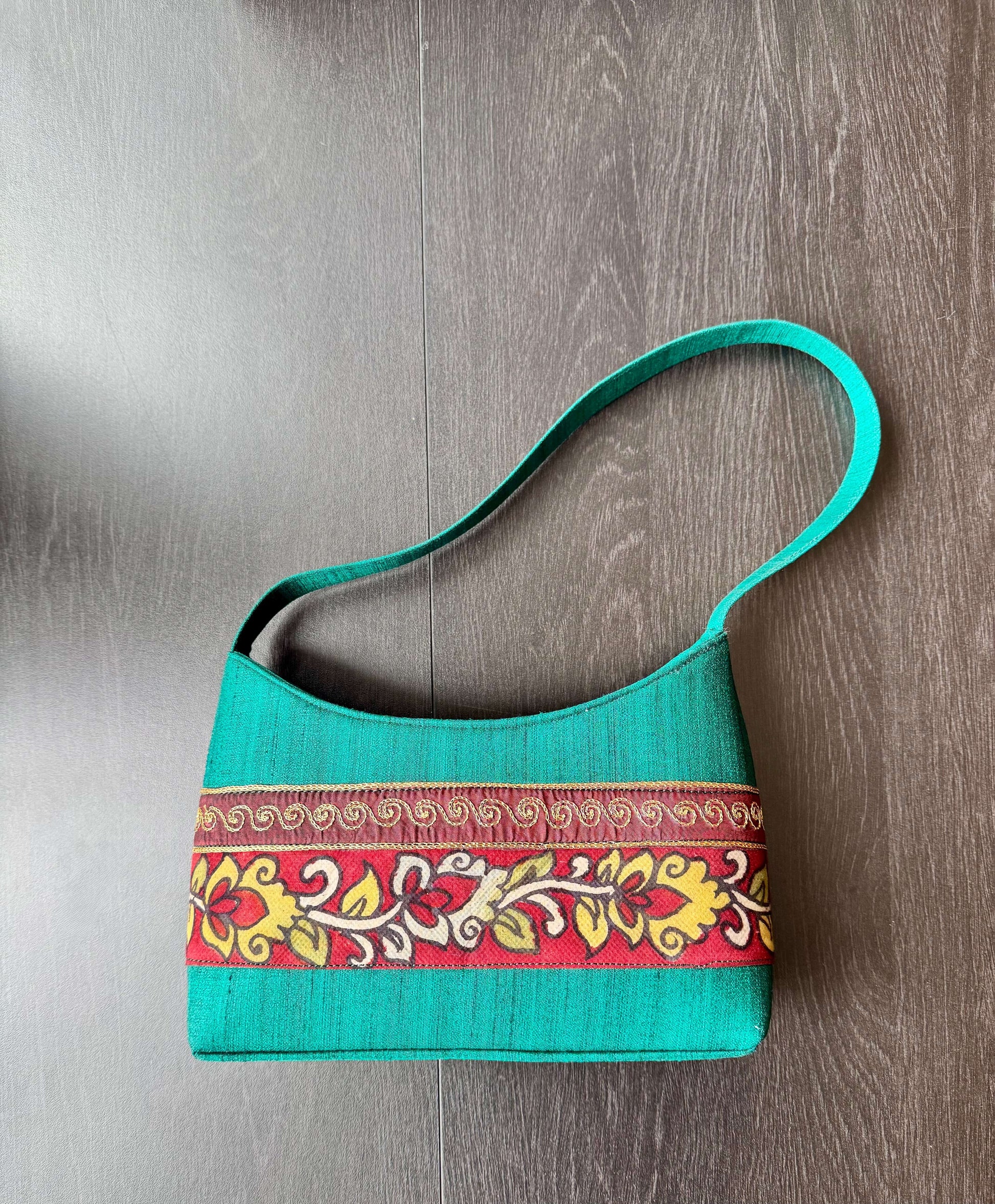 Turquoise handbag with a decorative band on a wooden surface