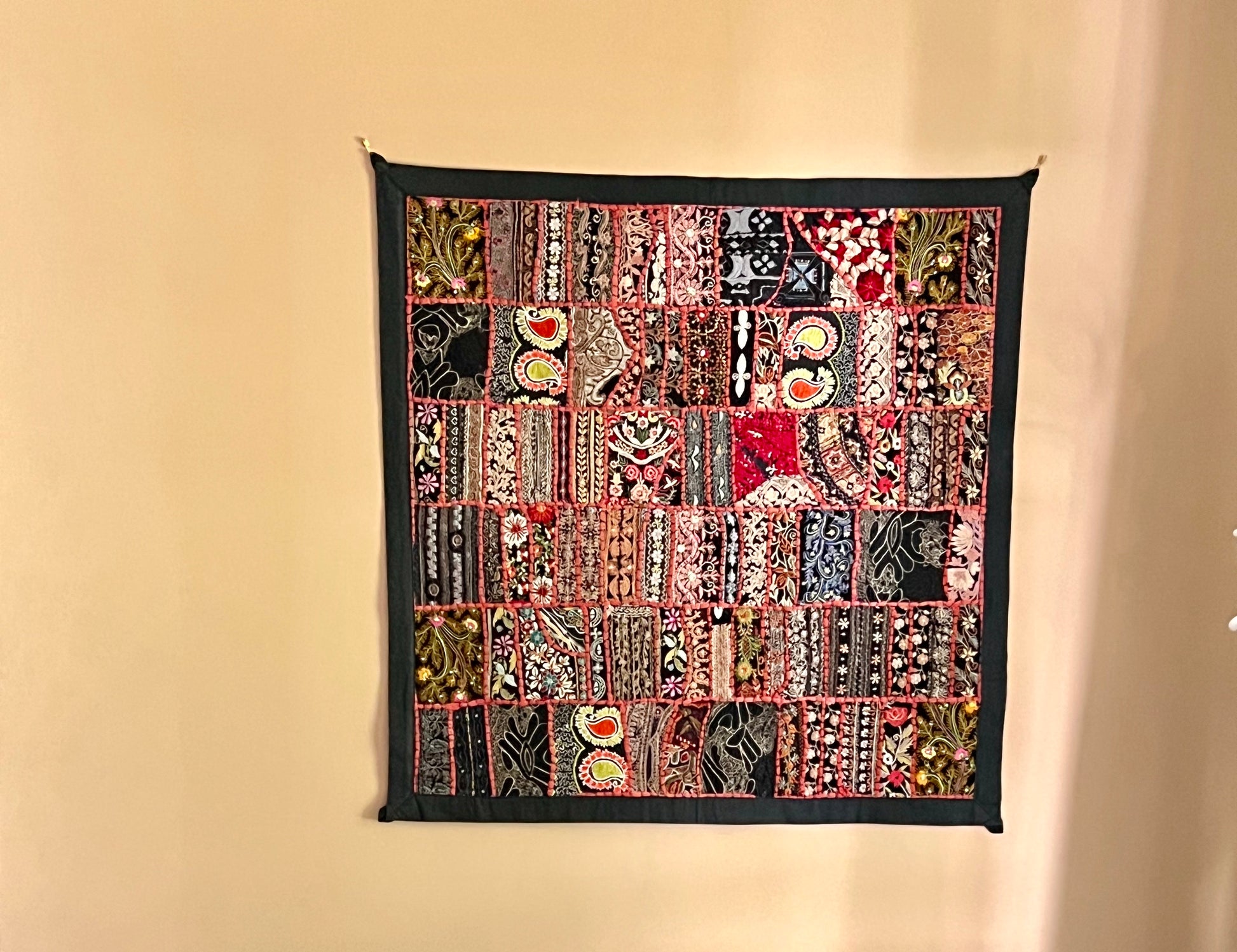 Khambhadia Patchwork quilt with various patterns and colors hanging on a beige wall.