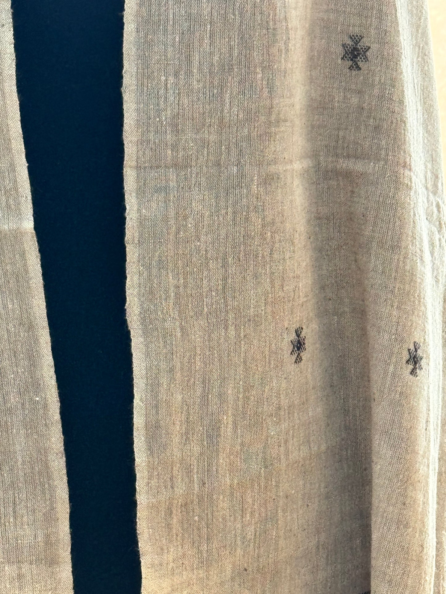 Textured off white surface of a stole with a dark black stripe and black abstract patterns.