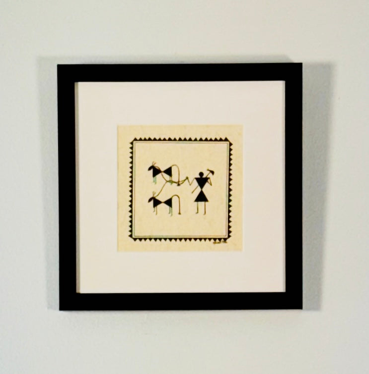 Framed Chittara folk art hand painted motif featuring black line drawings of horses and a figure on a cream background, matted in white and enclosed in a black frame against a light gray wall.