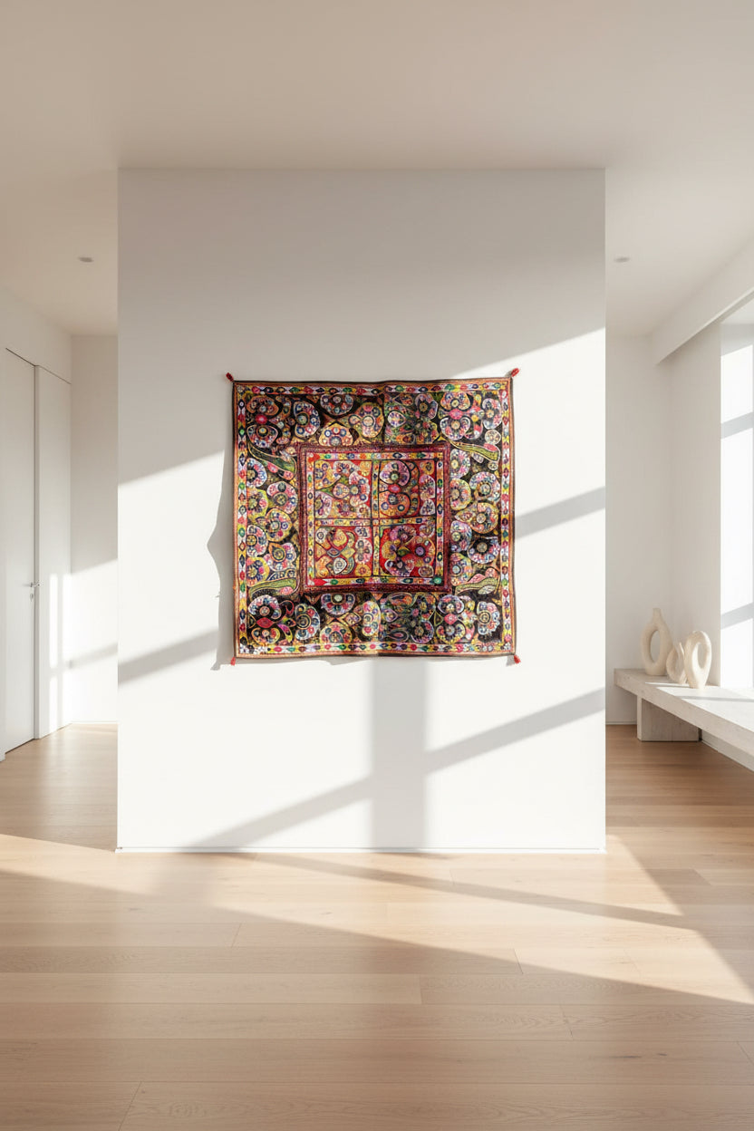 Colorful  Kutchi embroidered tapestry hanging on a white wall in a modern room with wooden floor and large windows.