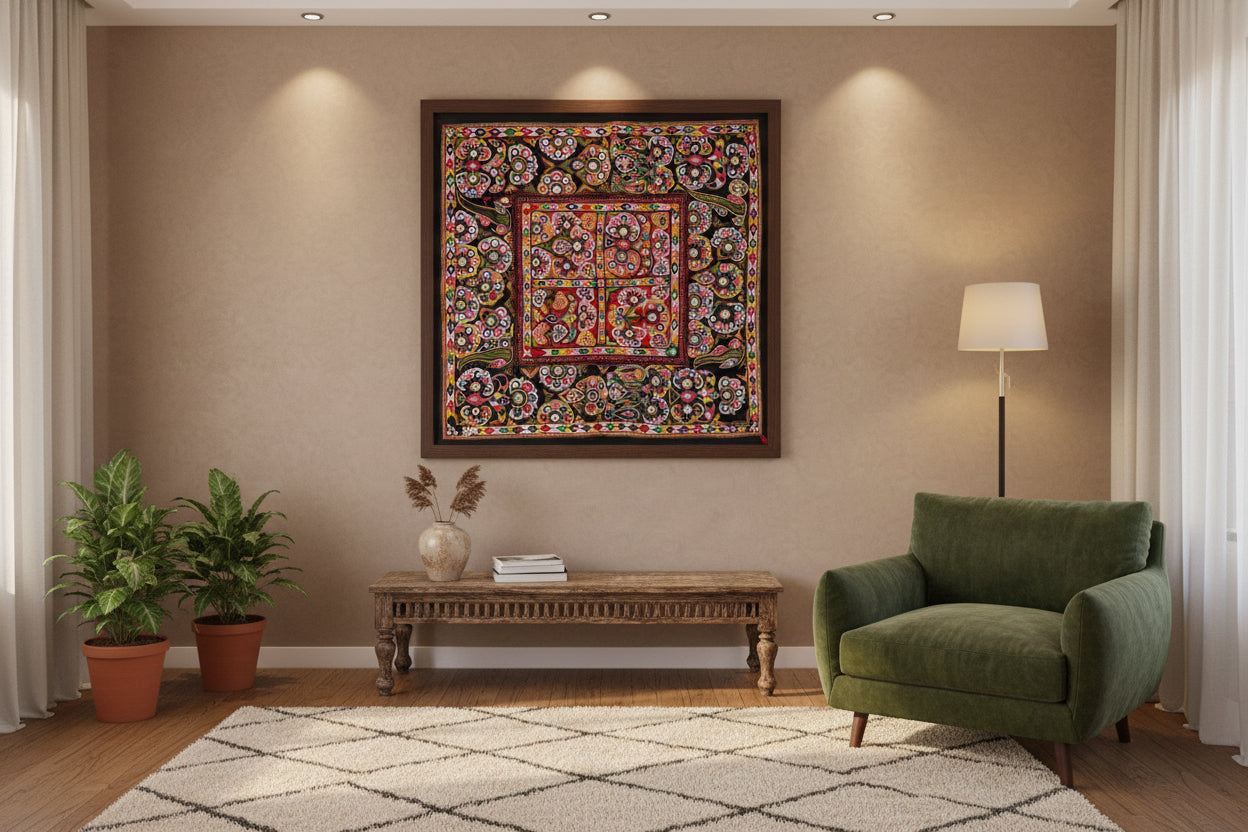 Kutchi embroidered textile in a frame on the wall with a green chair and a console table