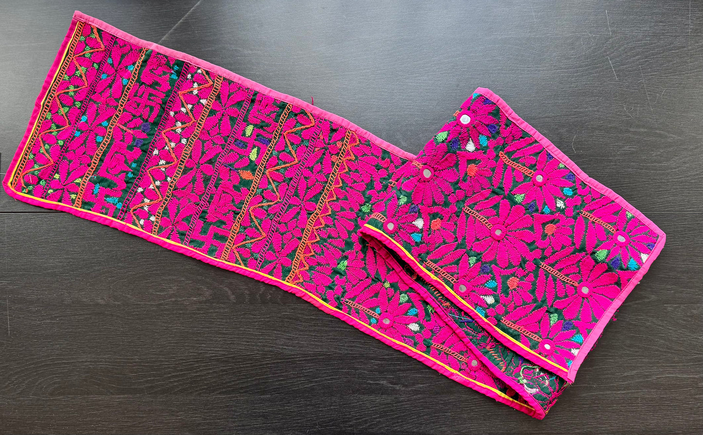 Pink Kutchi embroidered fabric on a dark wooden surface