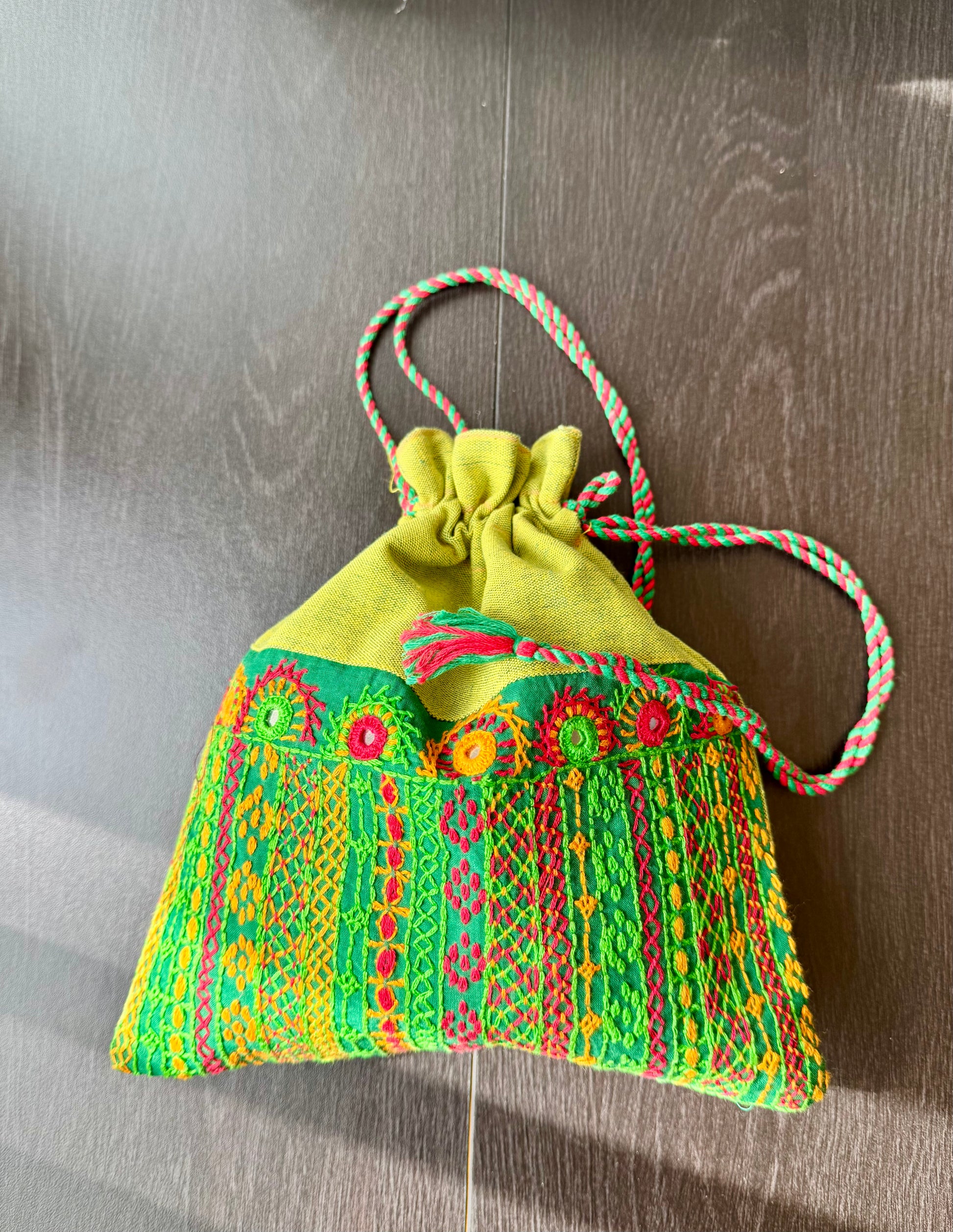 A traditional Lambani embroidery art potli bag with red, green, and beige colors, featuring geometric patterns and a drawstring closure.