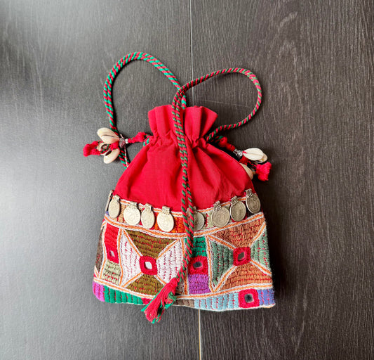 A traditional Lambani embroidery art potli bag with red, green, and beige colors, featuring geometric patterns and a drawstring closure.
